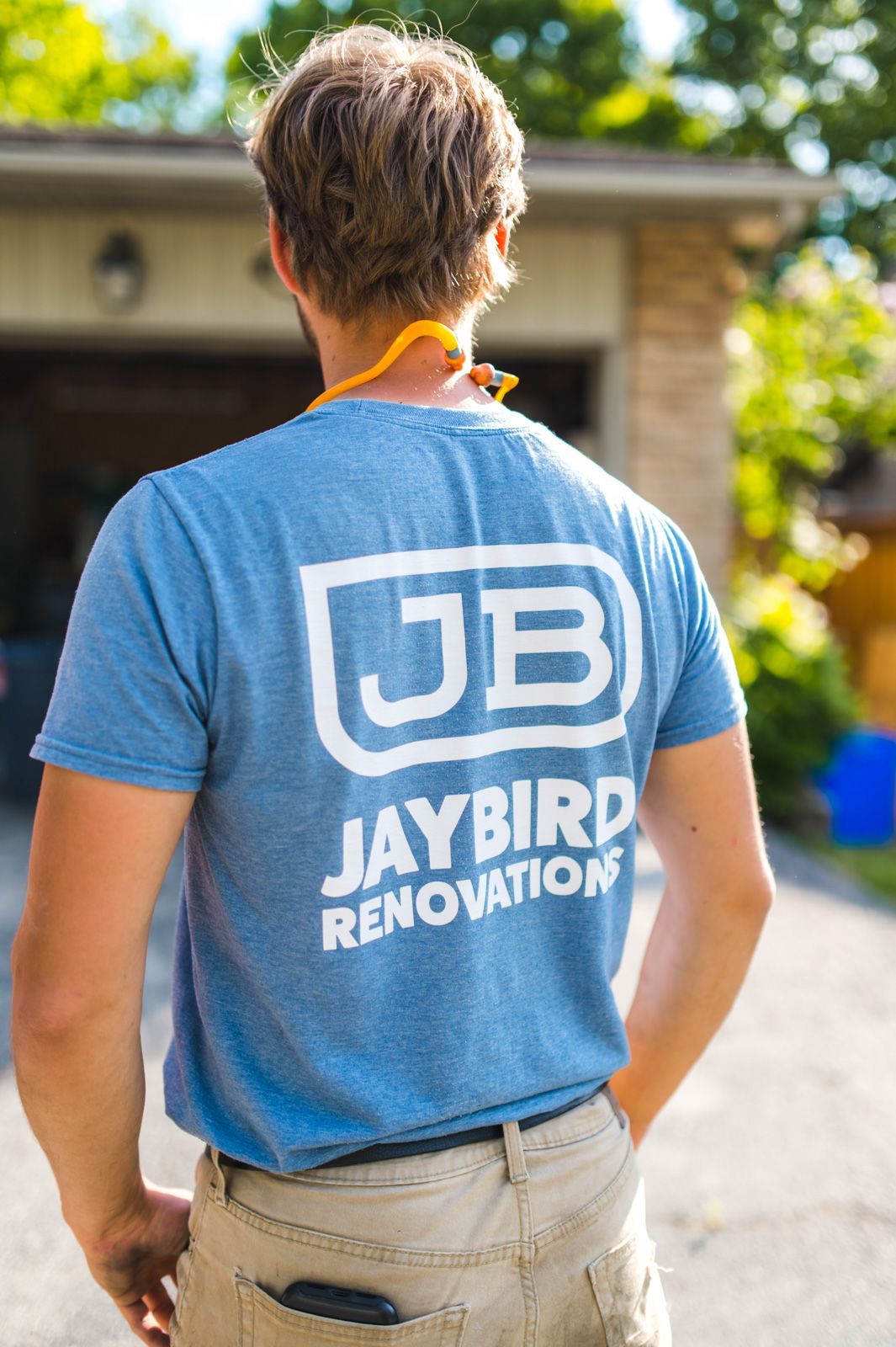 A man wearing a blue jaybird renovation t-shirt is standing in front of a garage.
