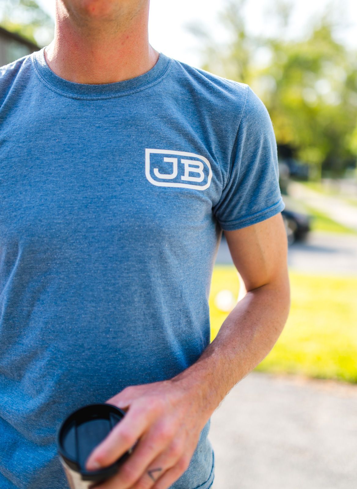 A man wearing a blue t-shirt with the letter jb on it is holding a cup.