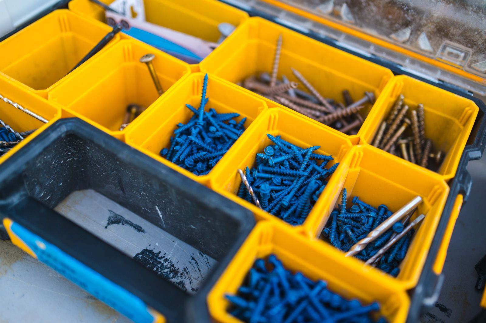 A yellow and black toolbox filled with blue screws and nails.