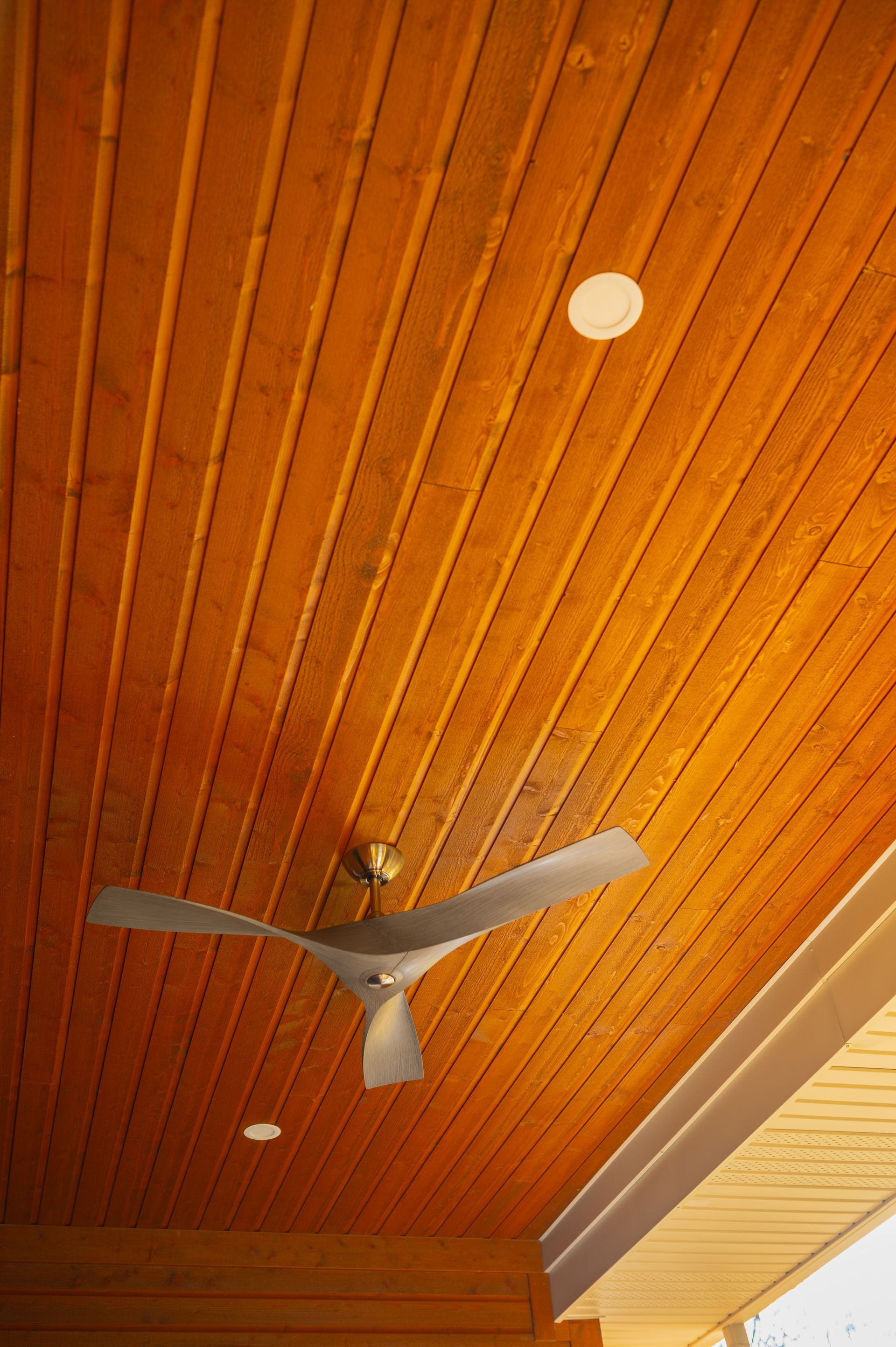 A ceiling fan is hanging from the ceiling of a wooden porch.