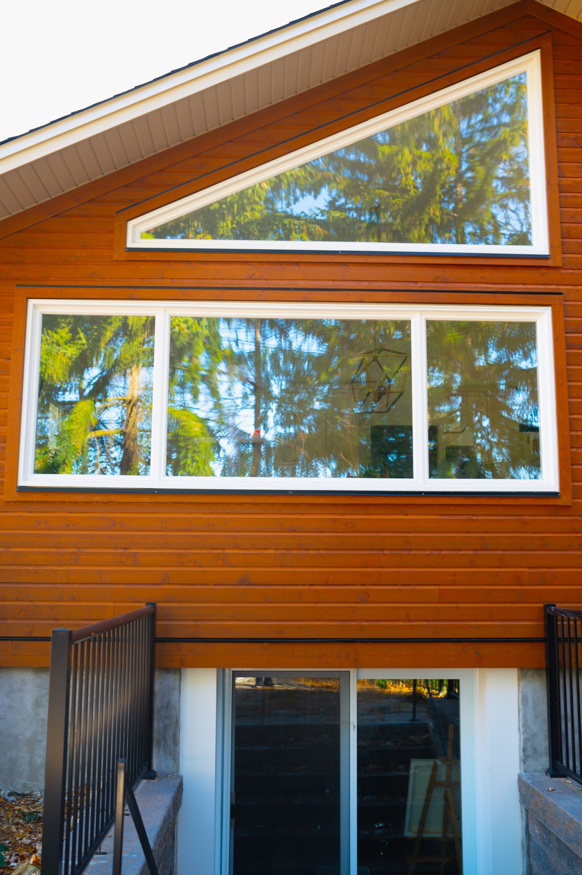 A large window on the side of a house with trees reflected in it.