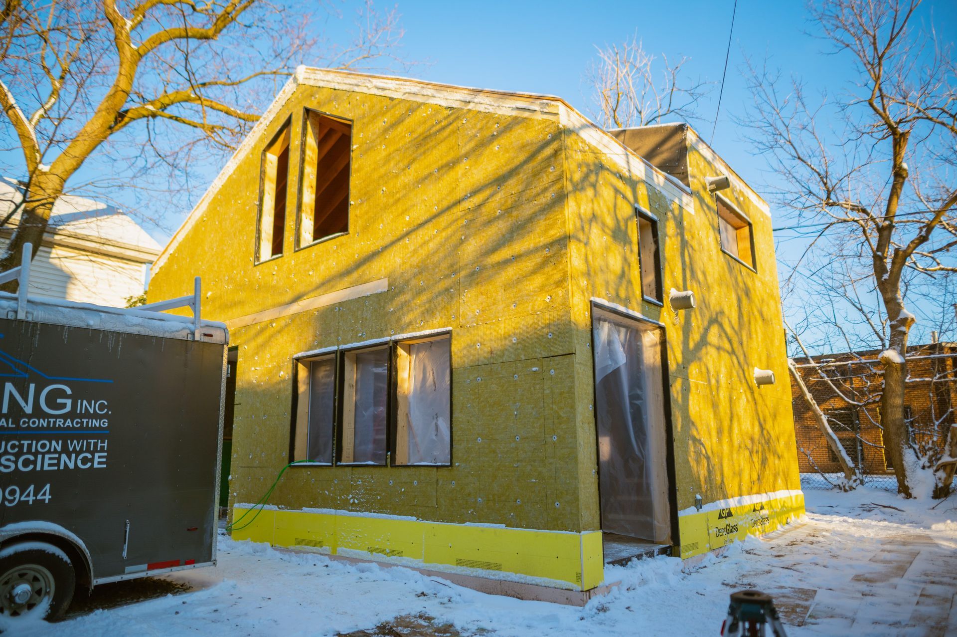 A house is being built in the snow next to a trailer.