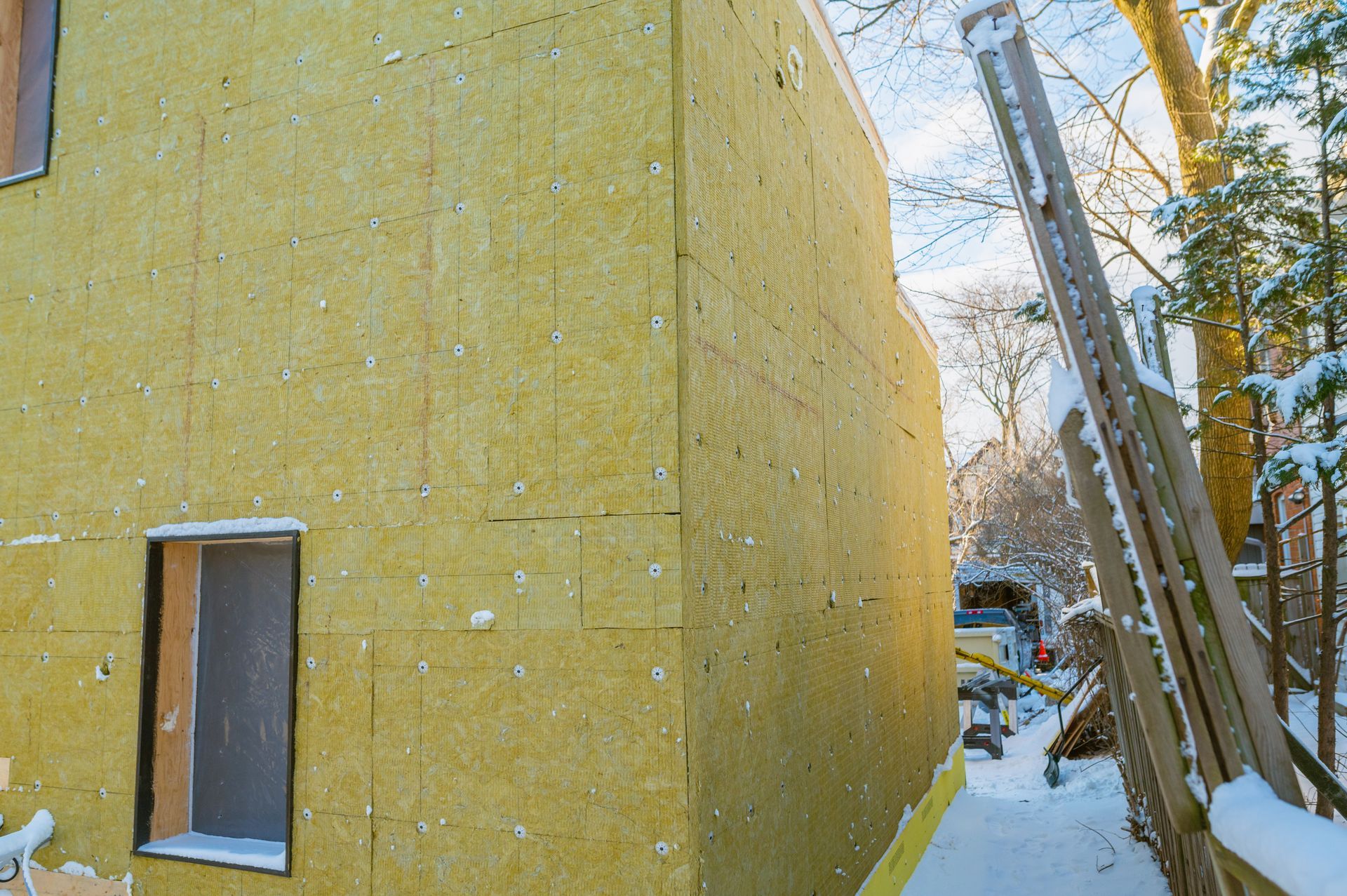 A yellow wall with a window and a ladder in the snow.