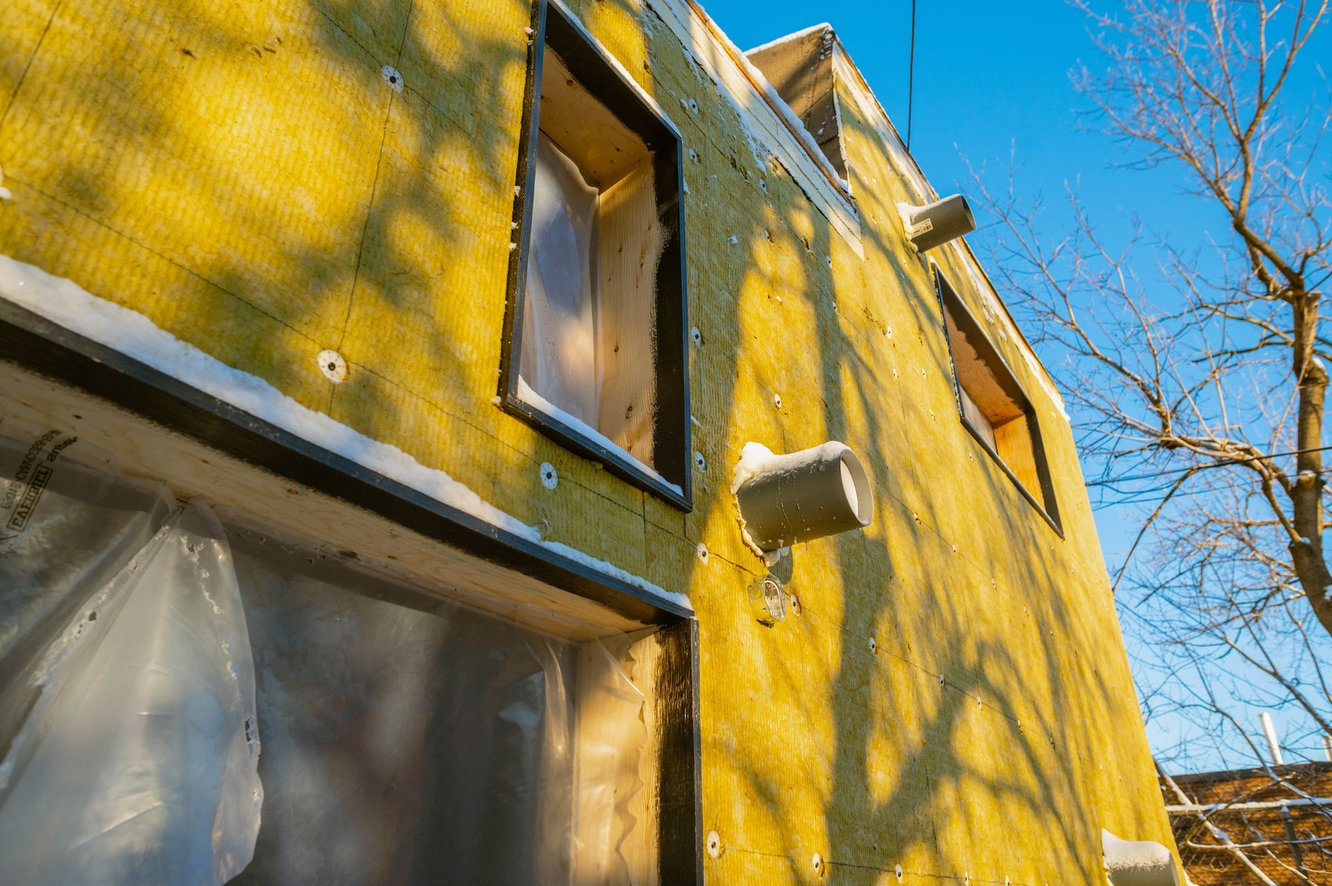 A house is being built with yellow insulation and a window.