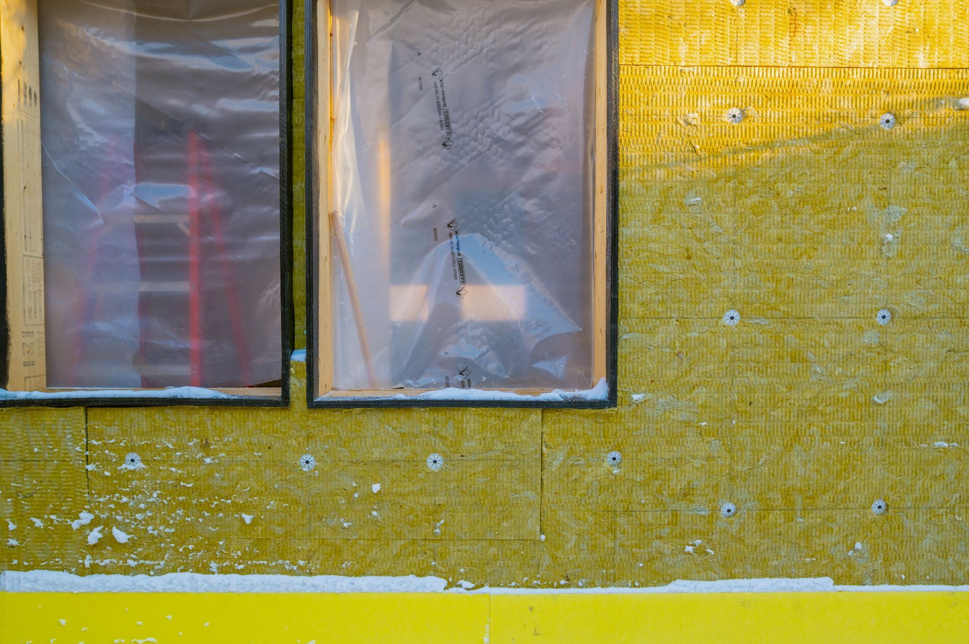 A building under construction with a yellow wall and two windows.