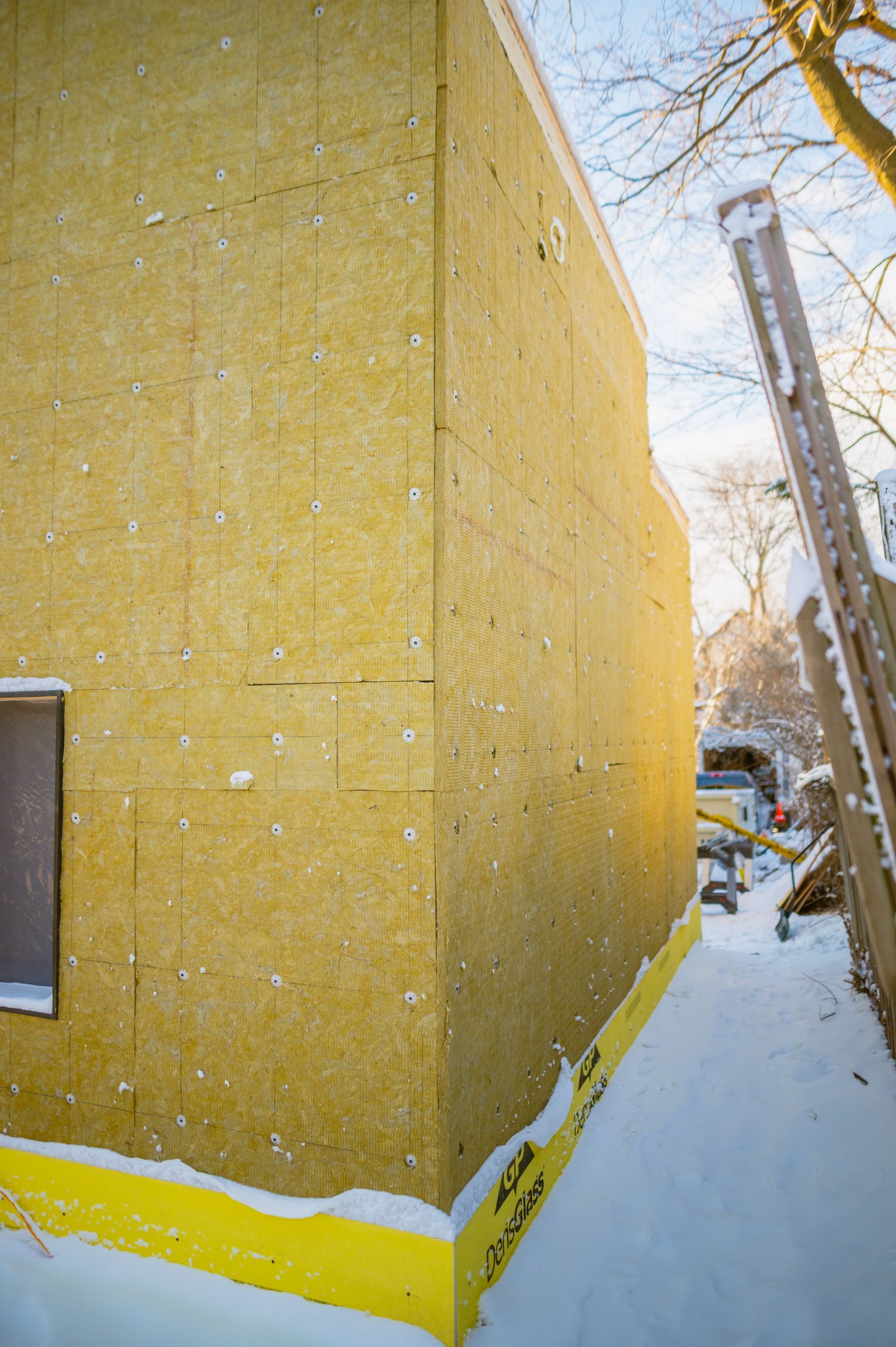 A building is being built in the snow with a ladder in the background.