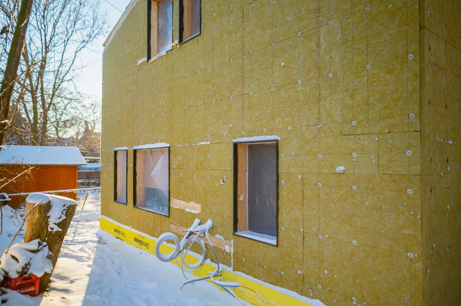 A house is being built in the snow with a bicycle parked in front of it.