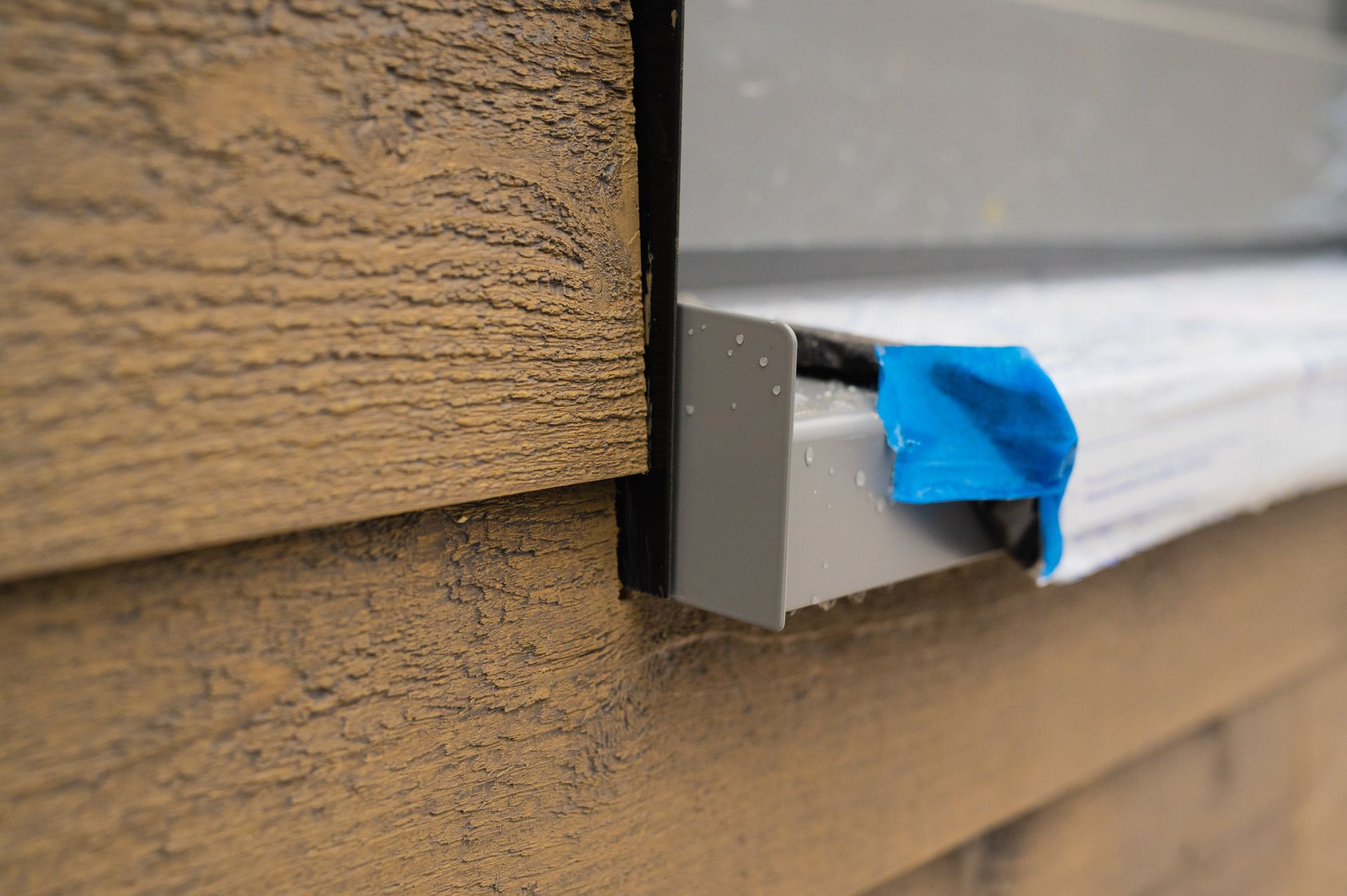 A close up of a window sill on a house with blue tape on it.