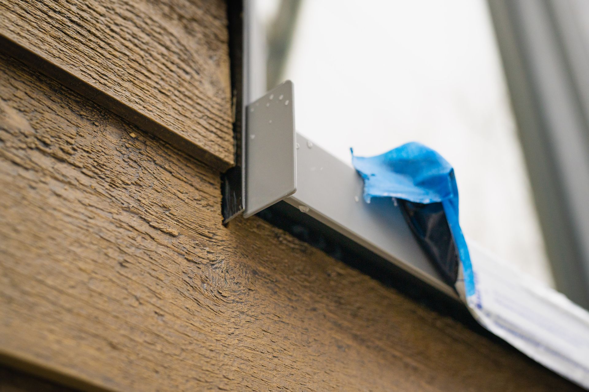 A close up of a window on a wooden wall with blue tape on it.