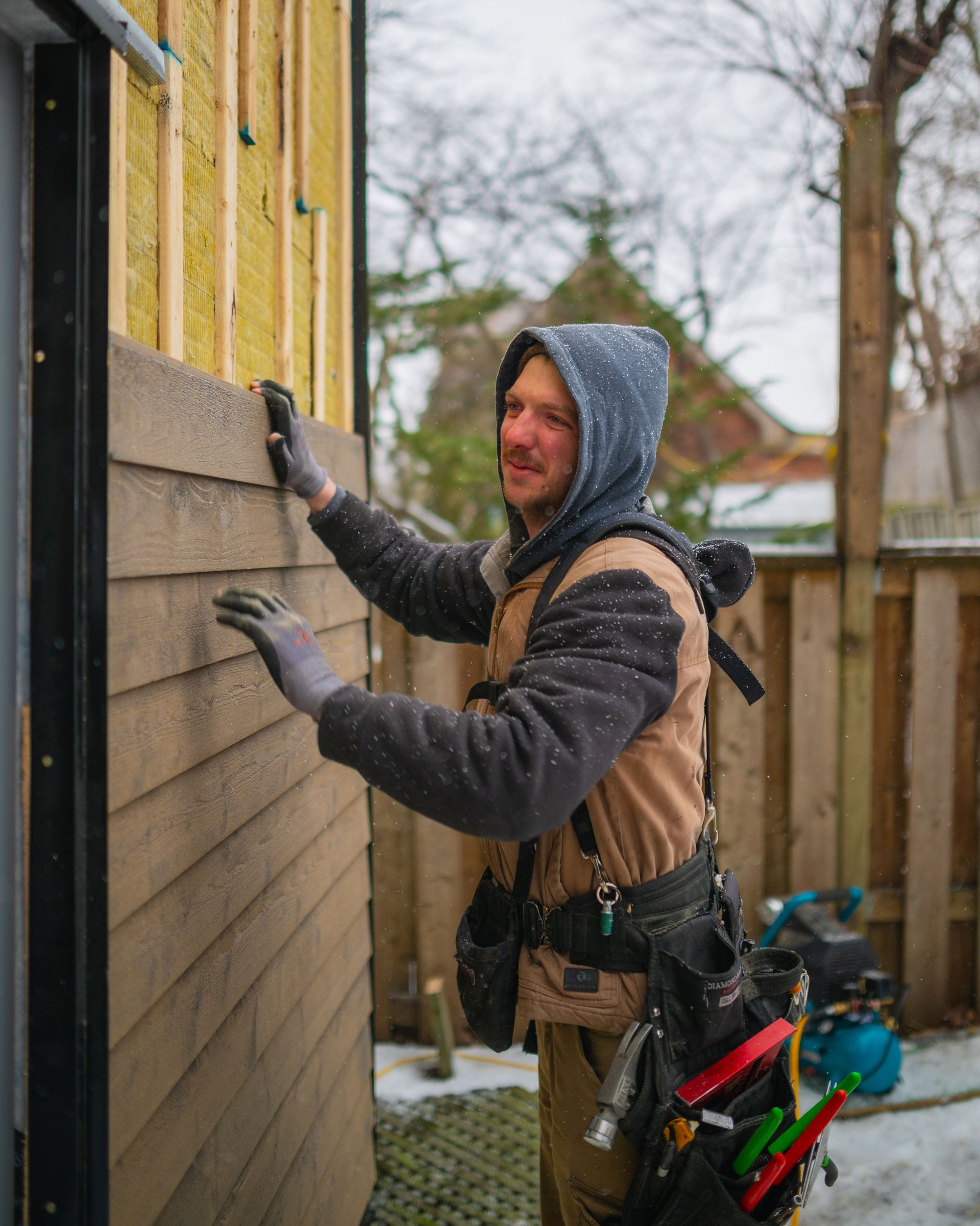 A man in a hooded jacket is working on a wooden wall.
