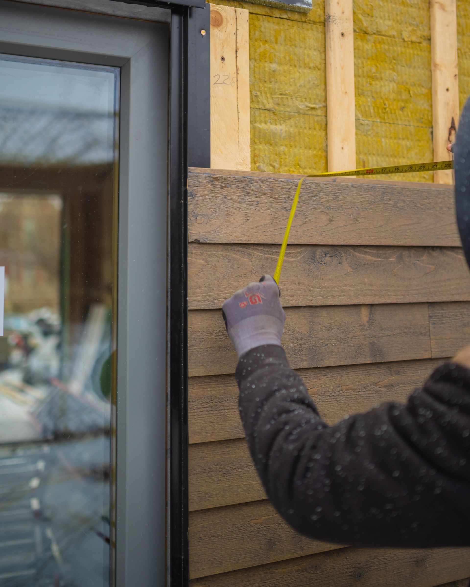 A man is measuring a wooden wall with a tape measure.