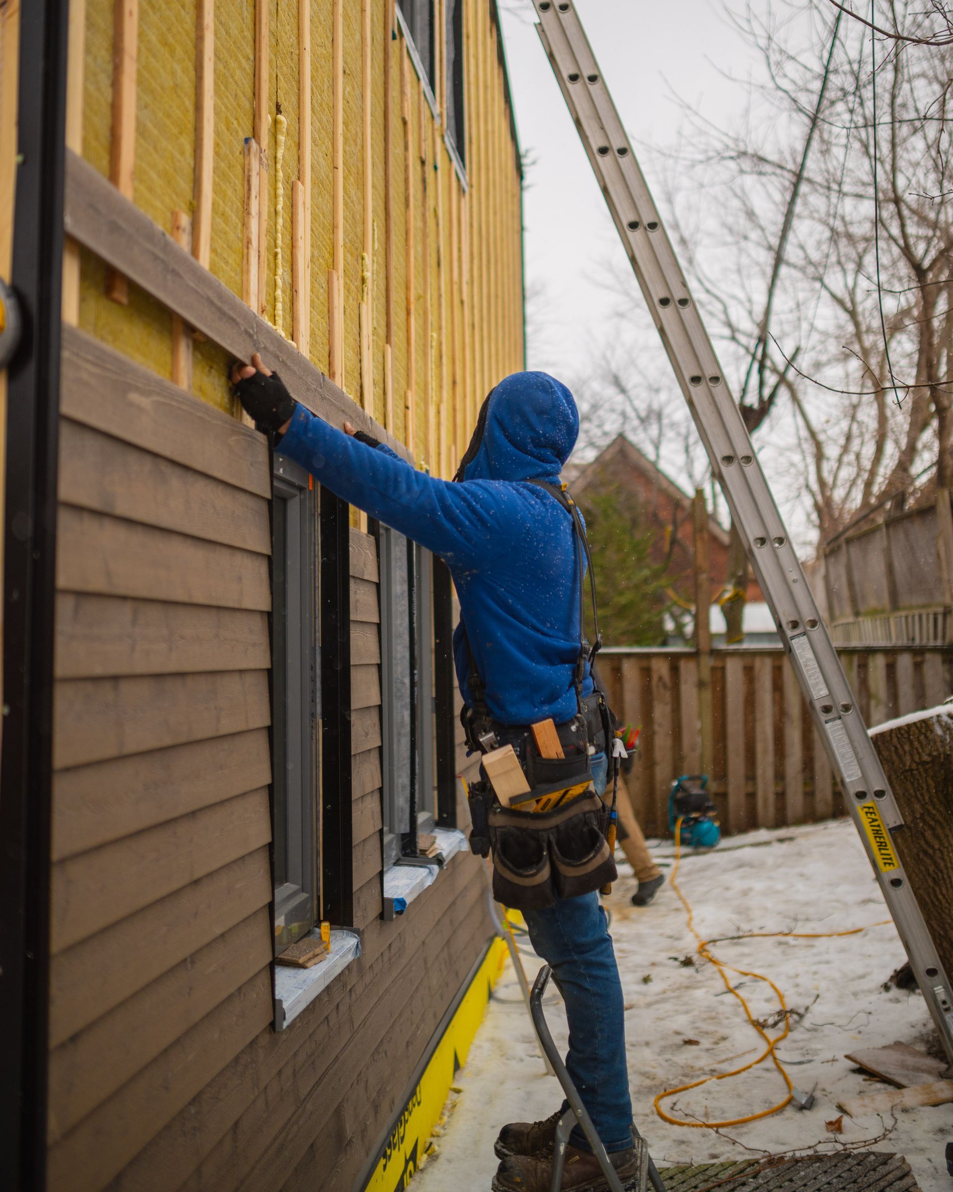 A man is standing next to a ladder on the side of a building.