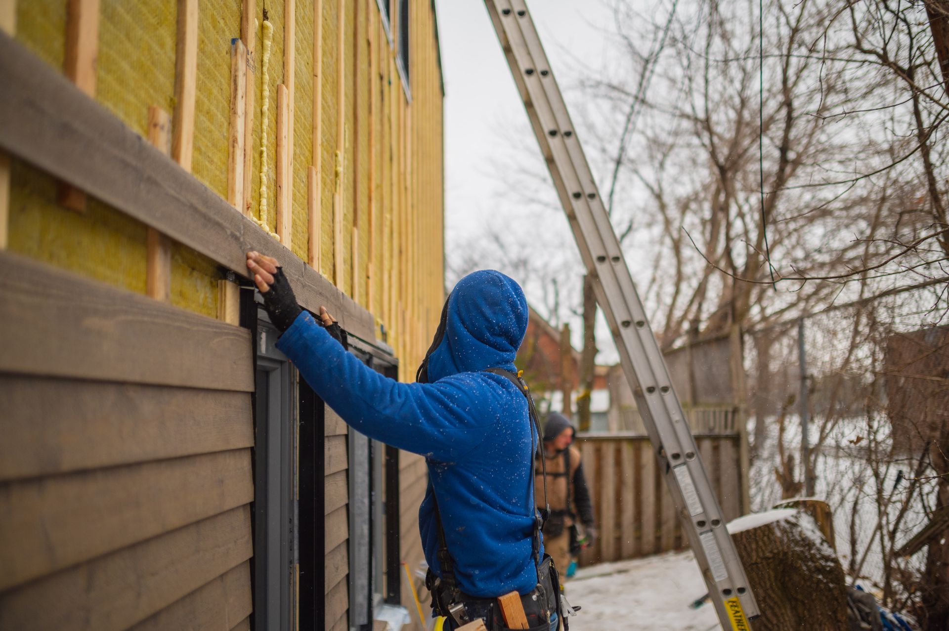 A man in a blue jacket is working on the side of a house.