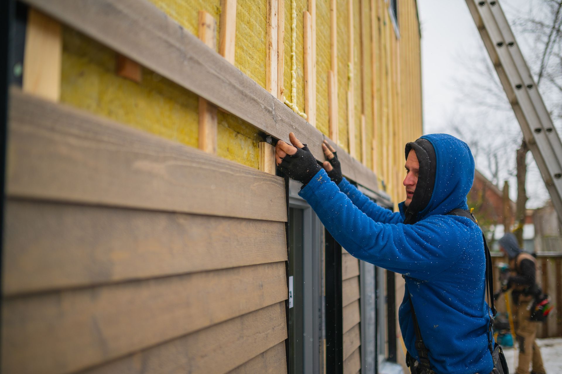 A man in a blue jacket is working on a wooden wall.