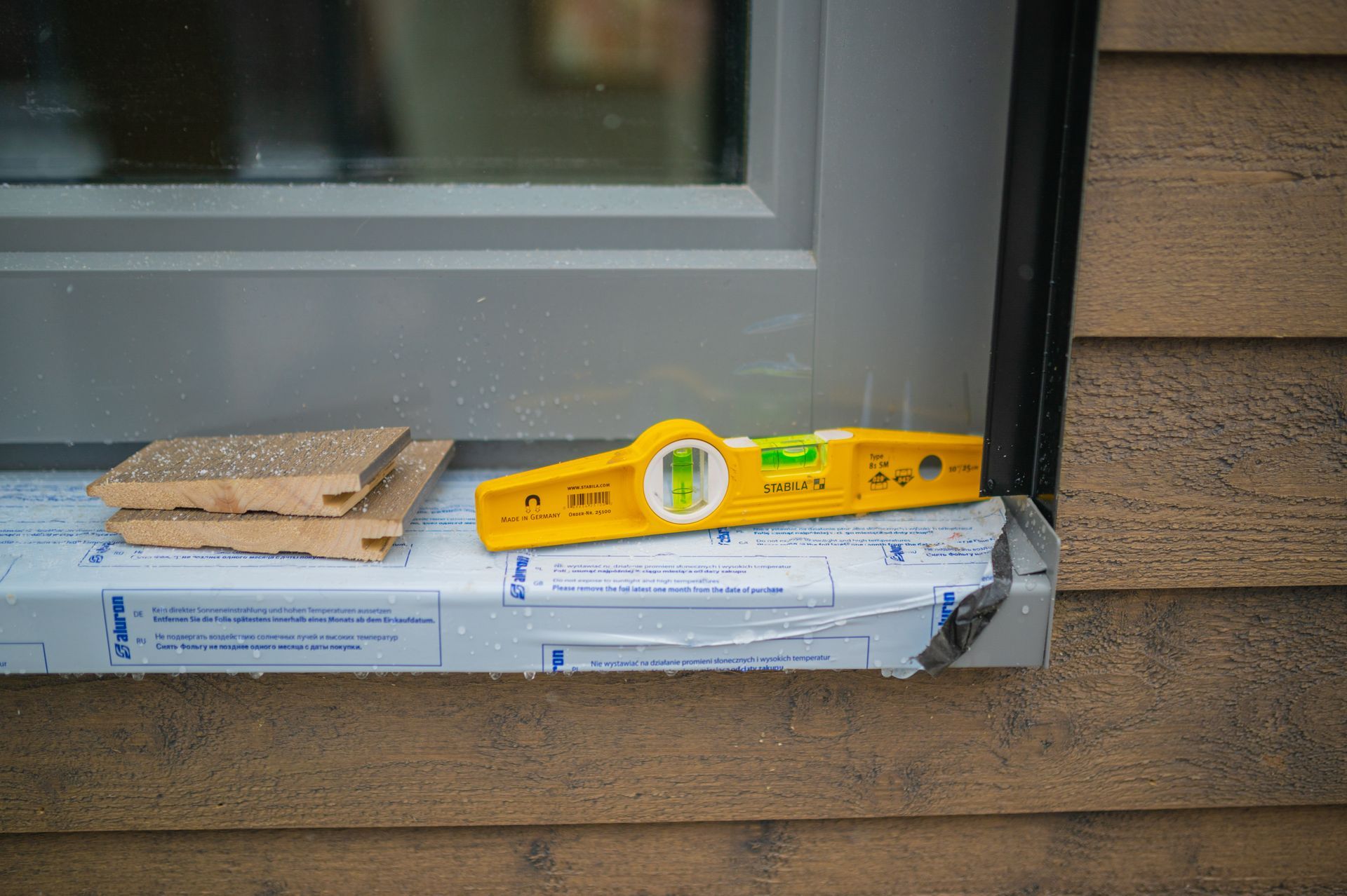 A yellow level is sitting on a window sill next to a window.