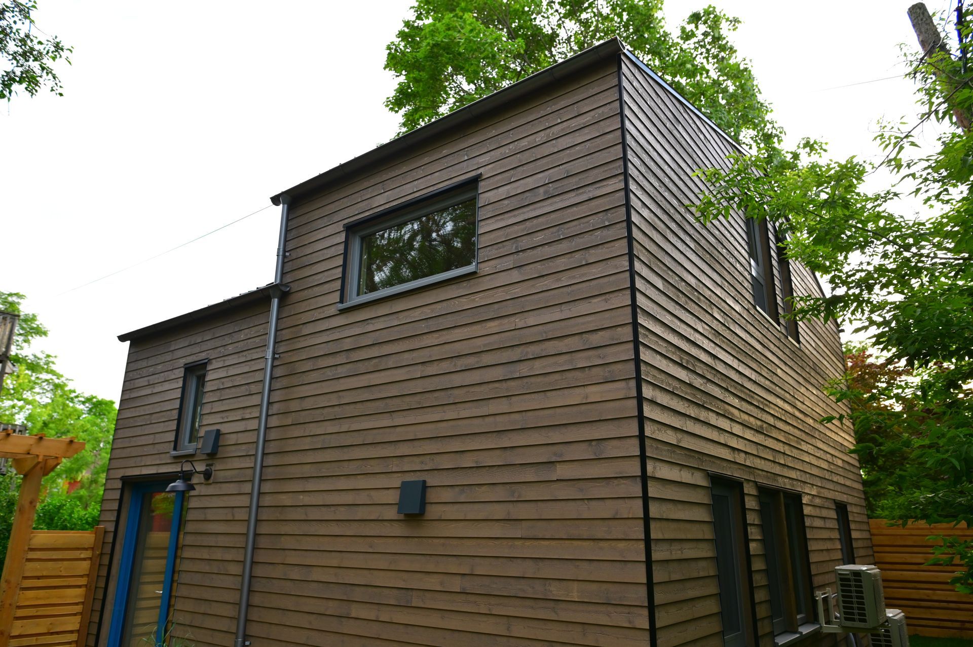 A brown house with a blue door is surrounded by trees