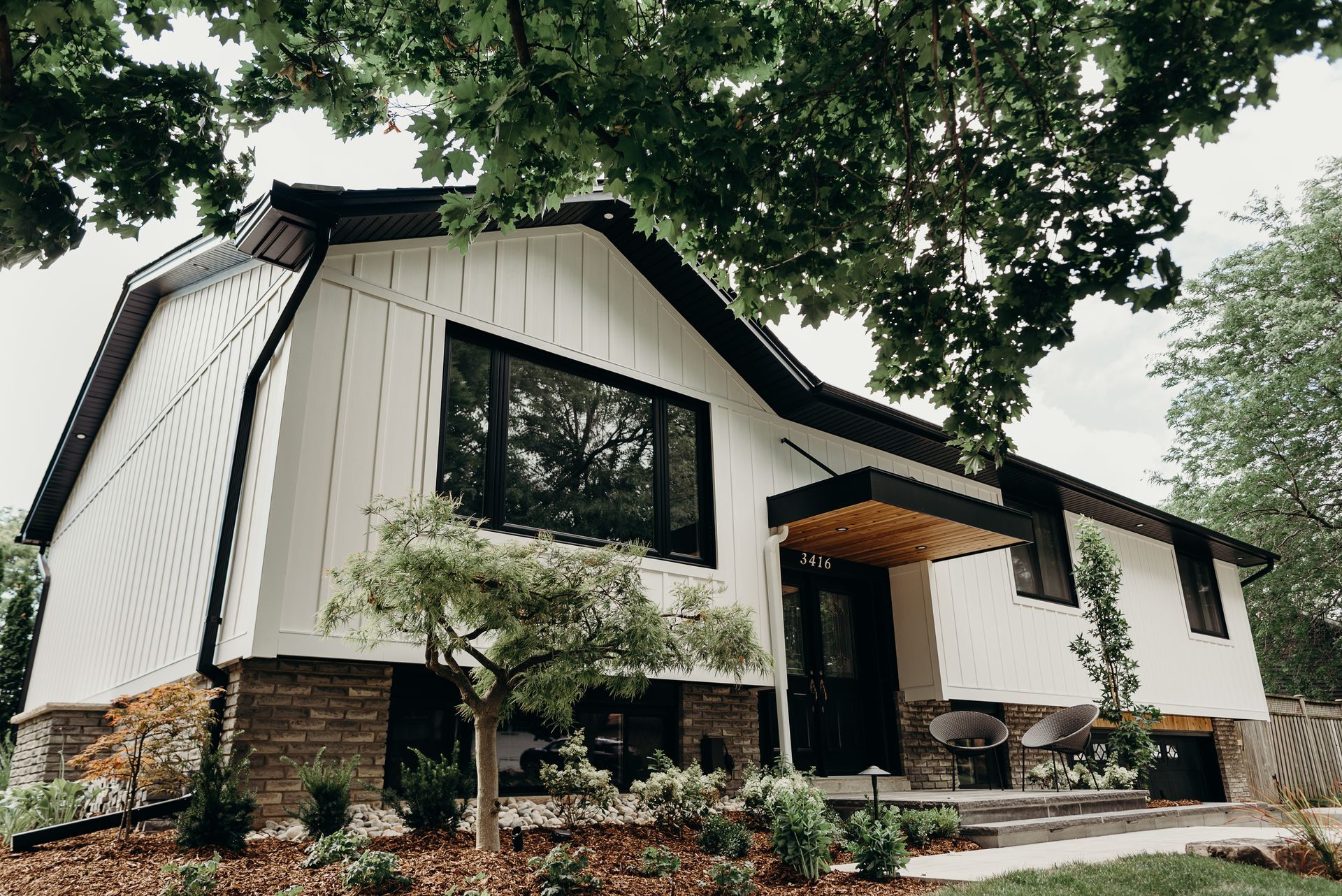 A white house with a black roof is surrounded by trees.
