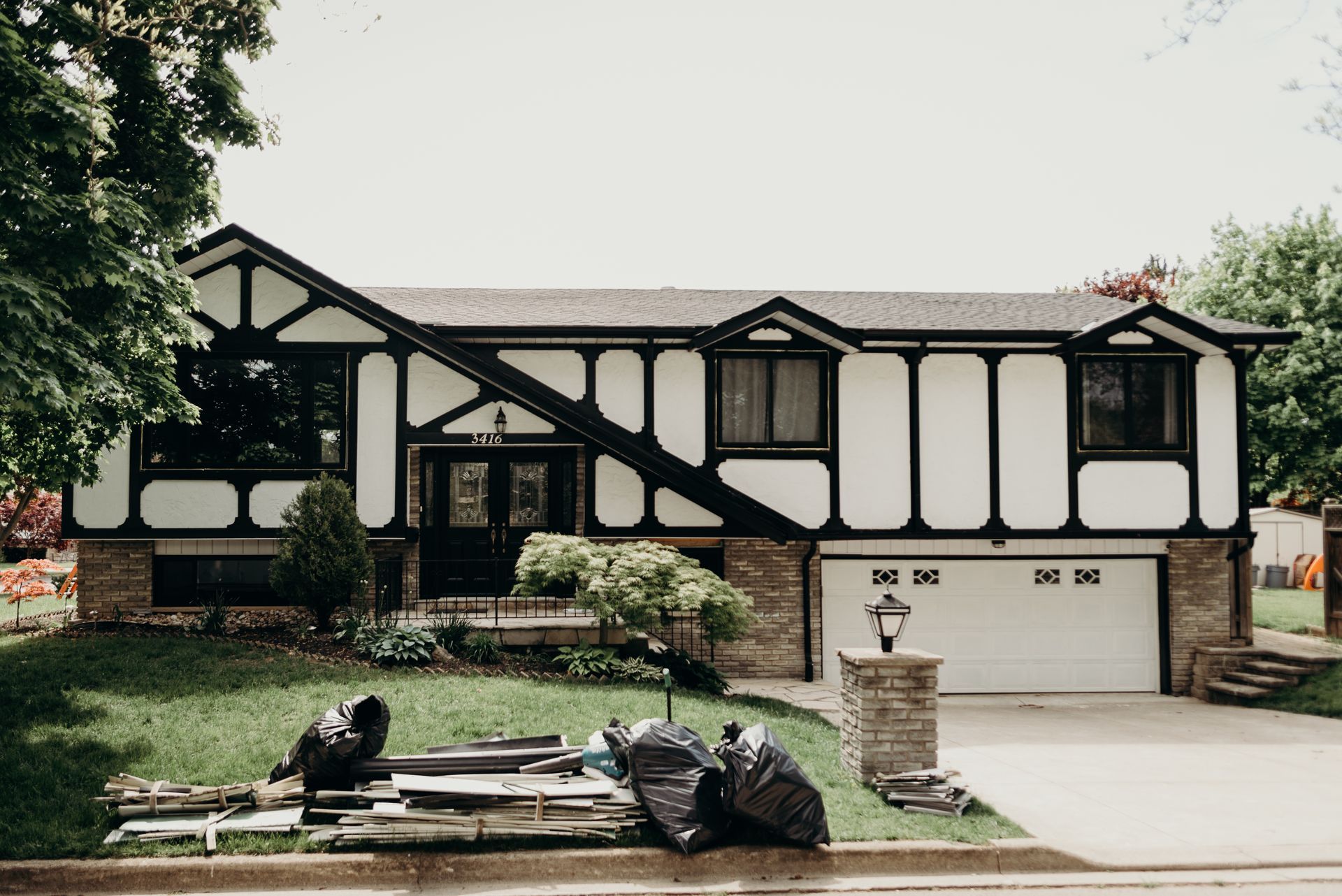 A black and white house with a lot of trash in front of it.