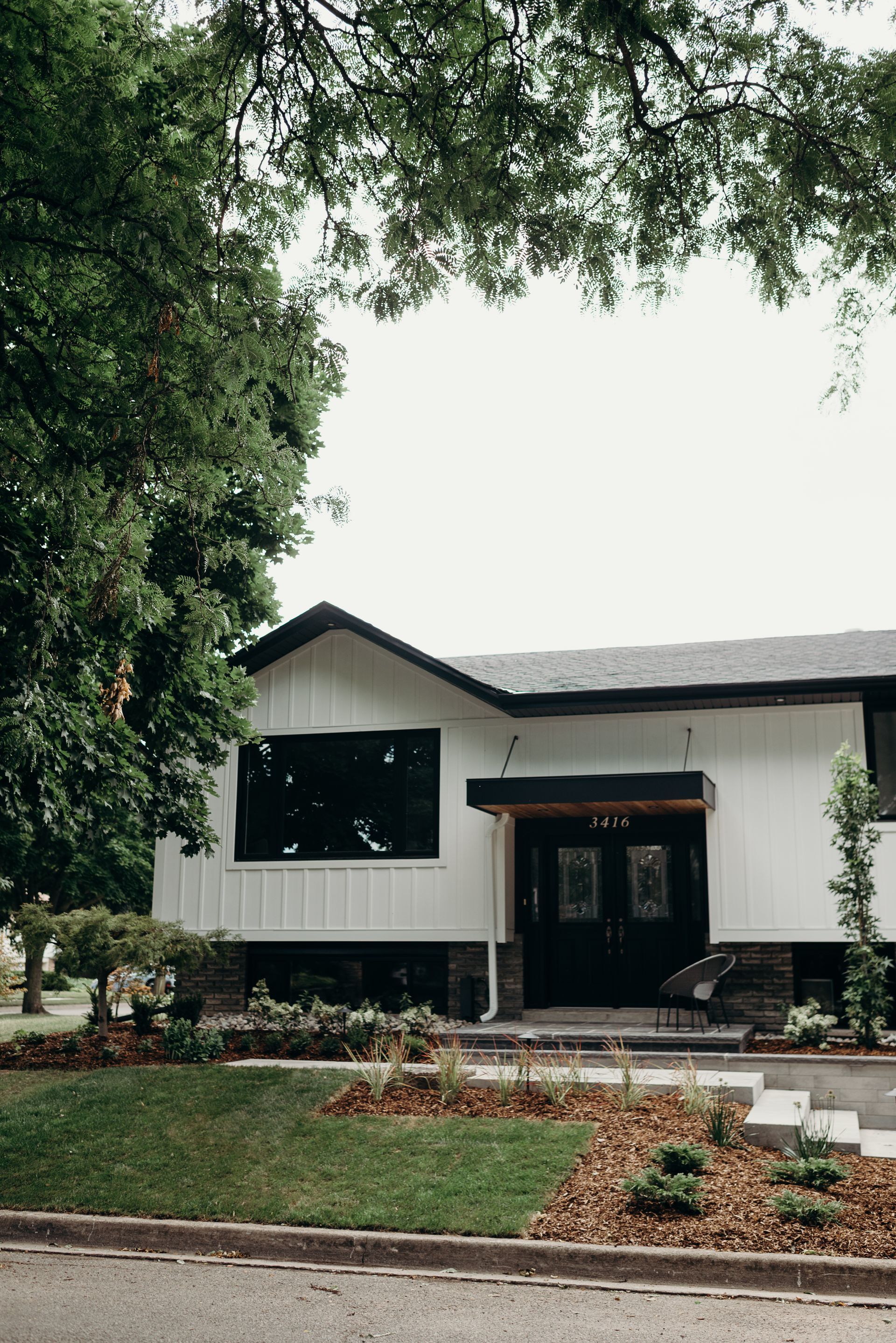 A white house with a black door and a black roof is surrounded by trees.
