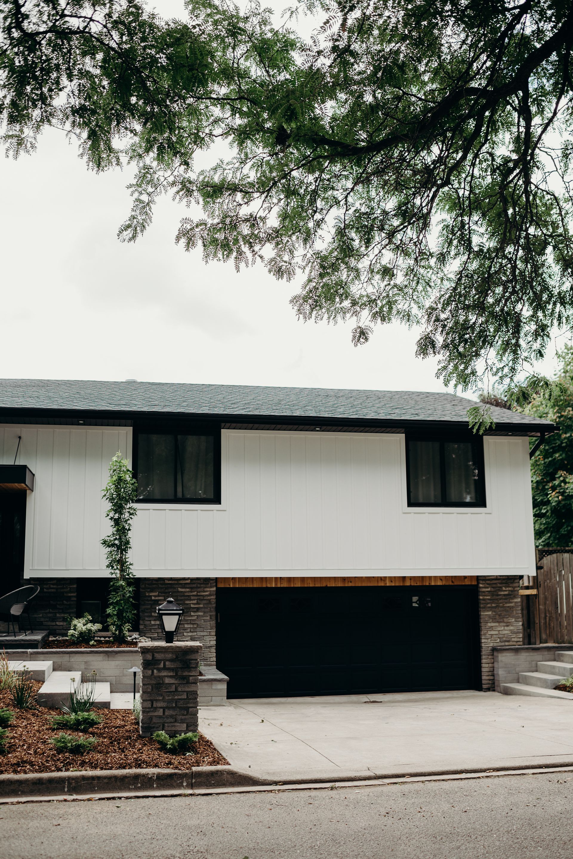 A white house with a black garage door and a tree in front of it.