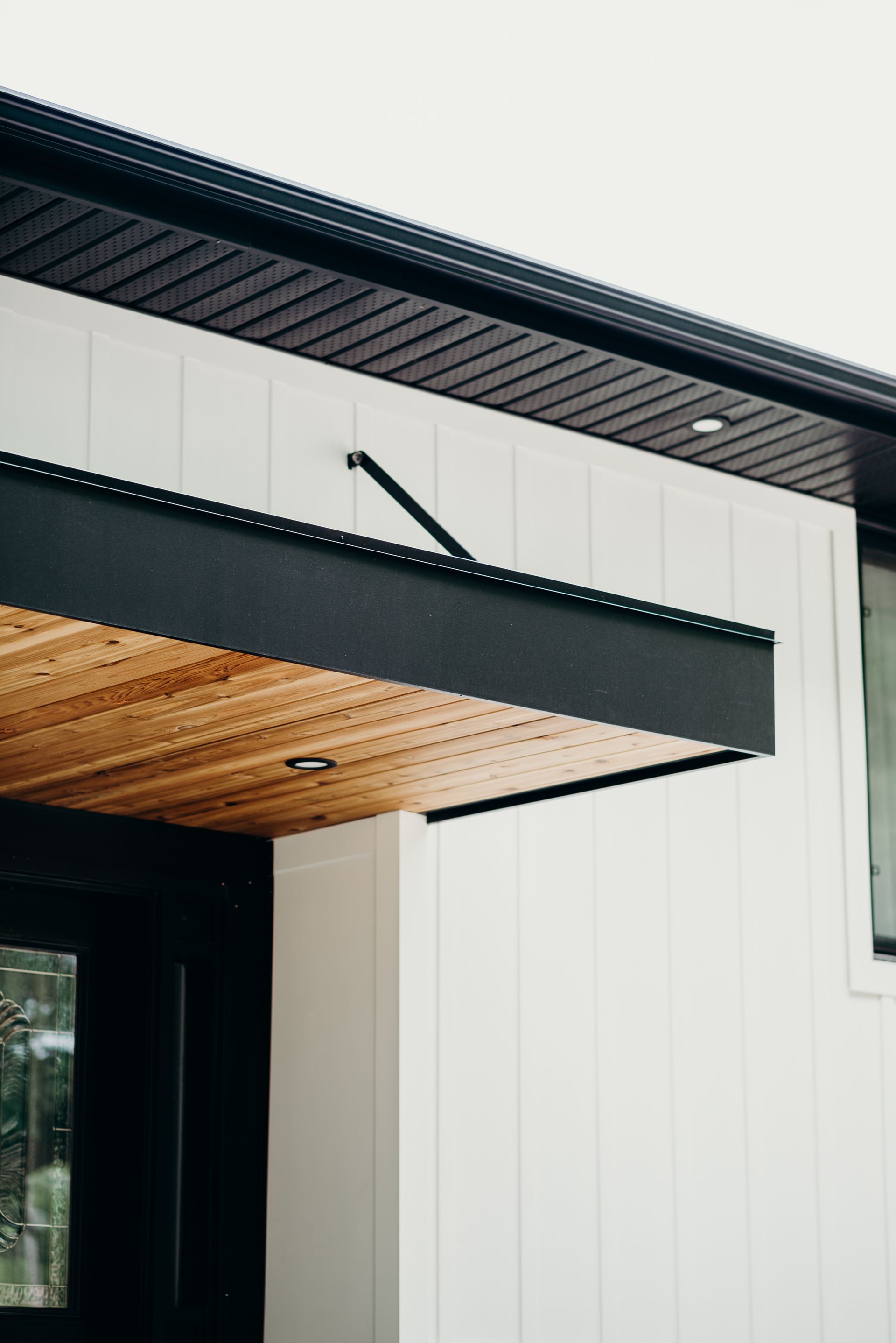 A white house with a black roof and a wooden canopy over the door.