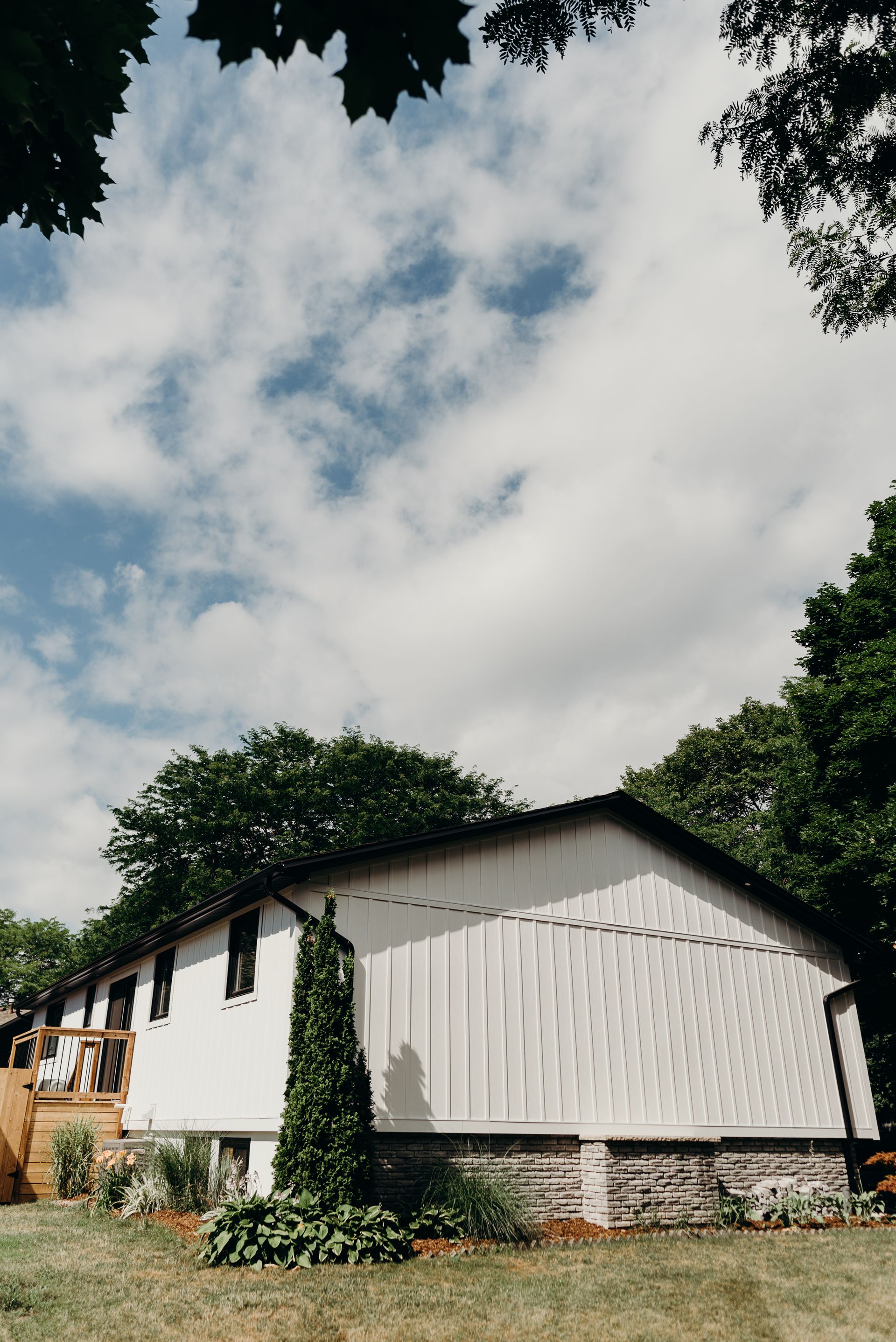 A white house with a black roof is surrounded by trees on a sunny day.