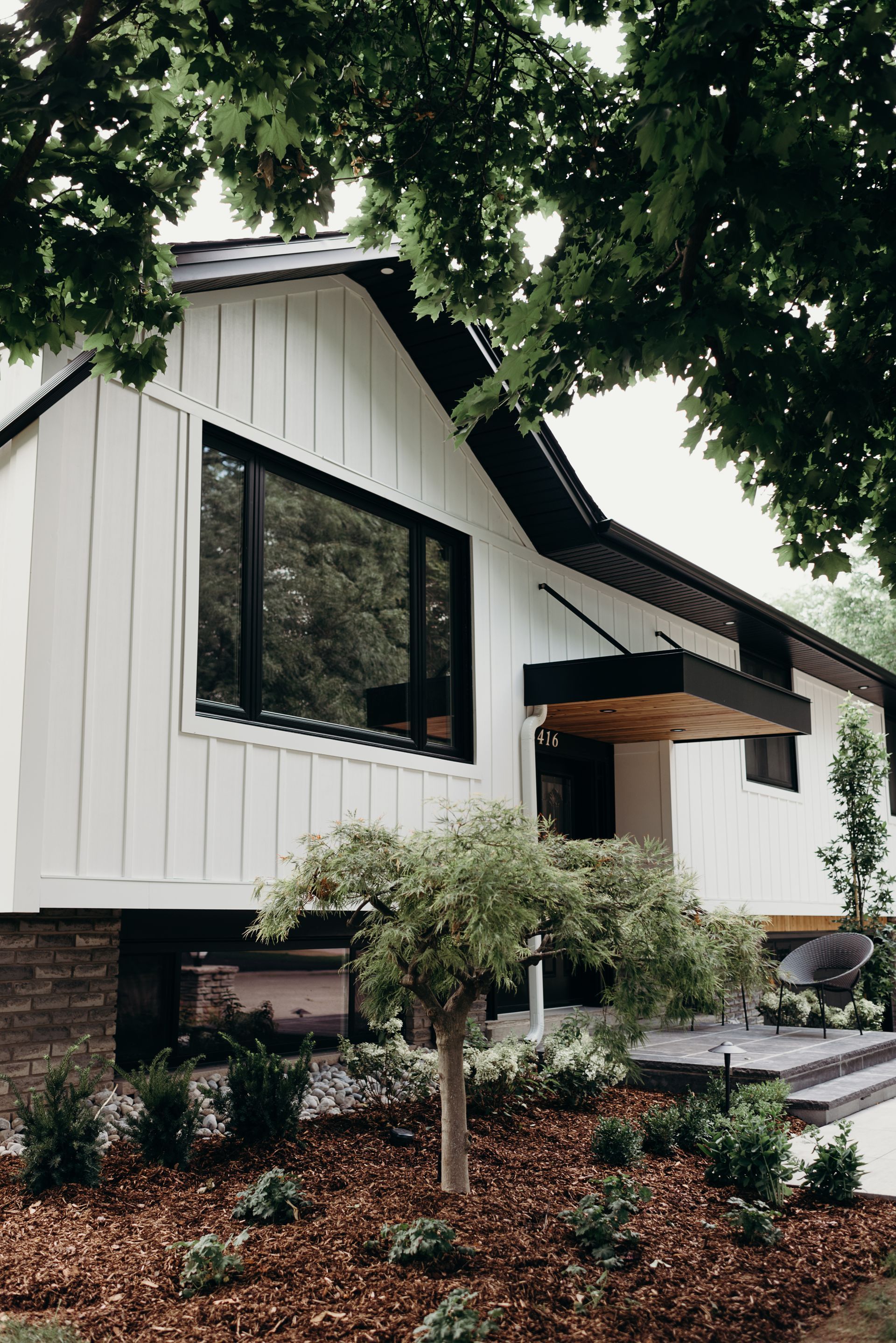 A white house with black windows and a tree in front of it.