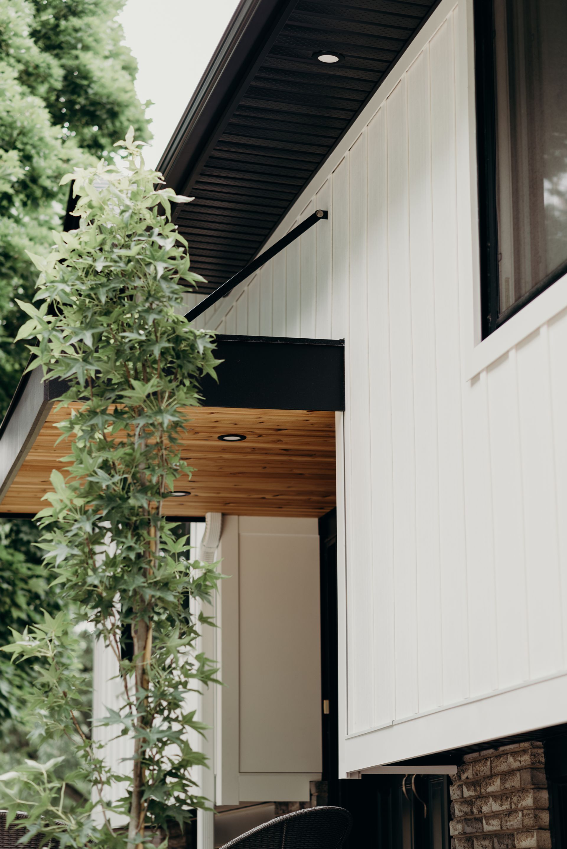 A white house with a wooden porch and a tree in front of it.