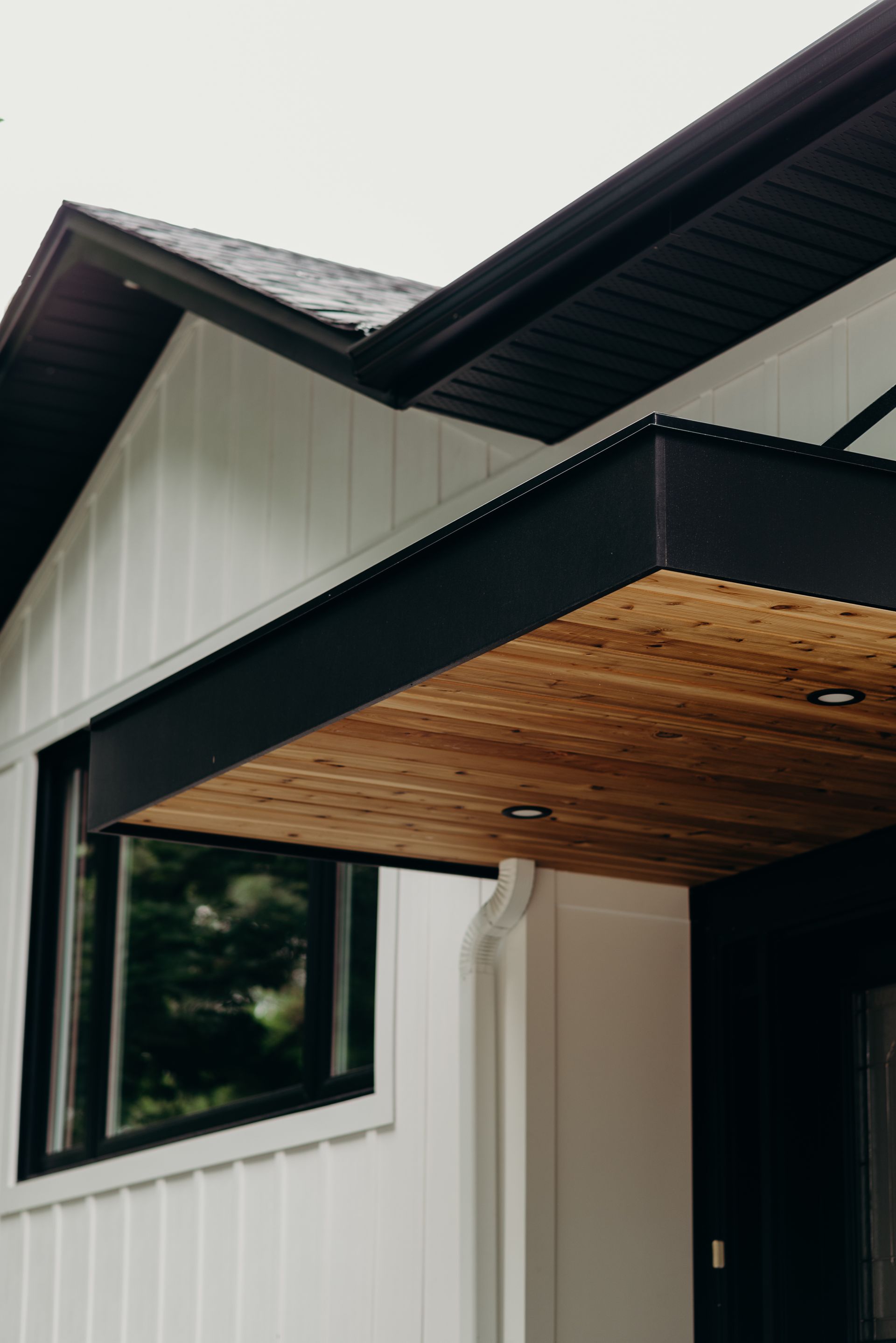 A white house with a black roof and a wooden porch.