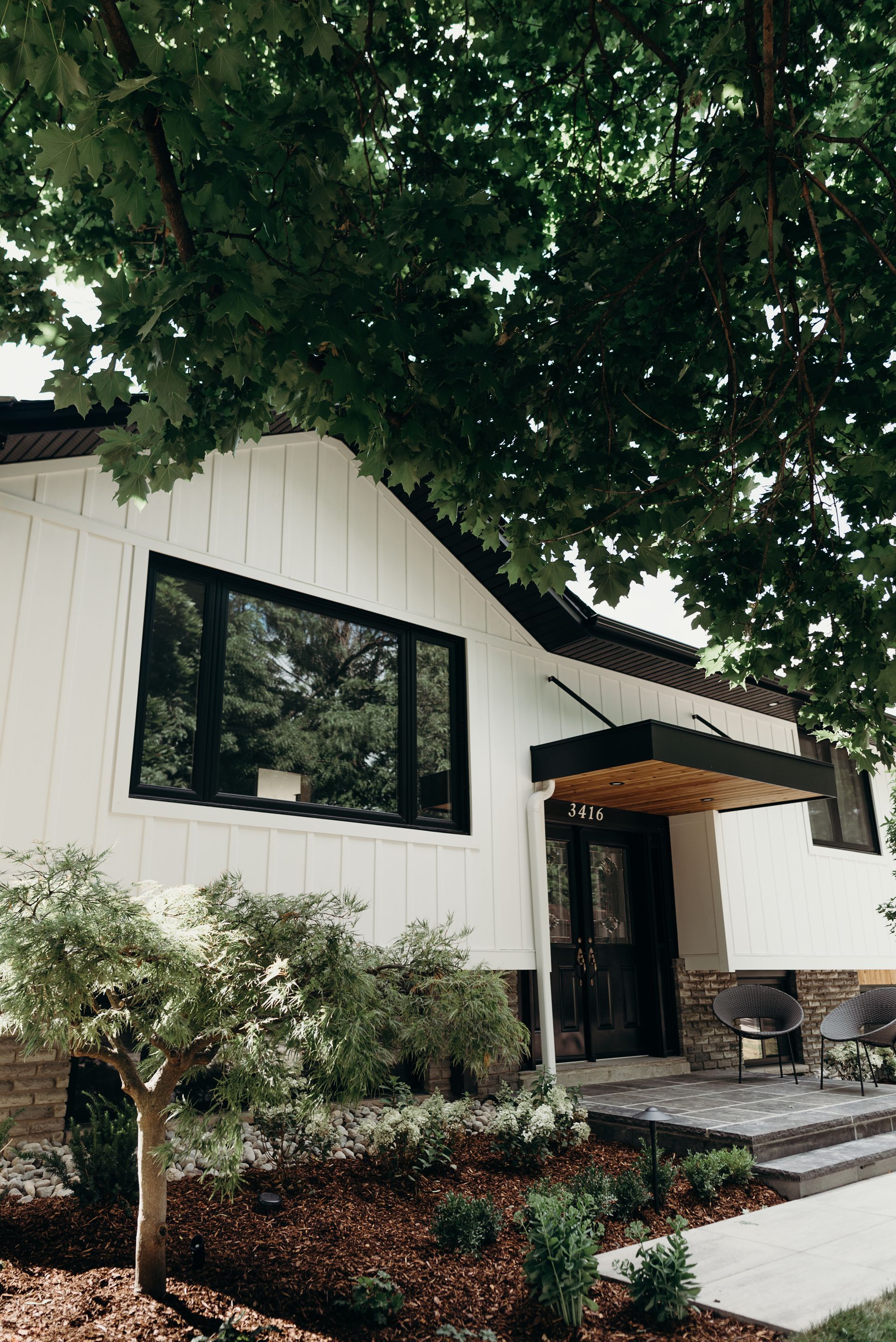A white house with black windows and a tree in front of it.