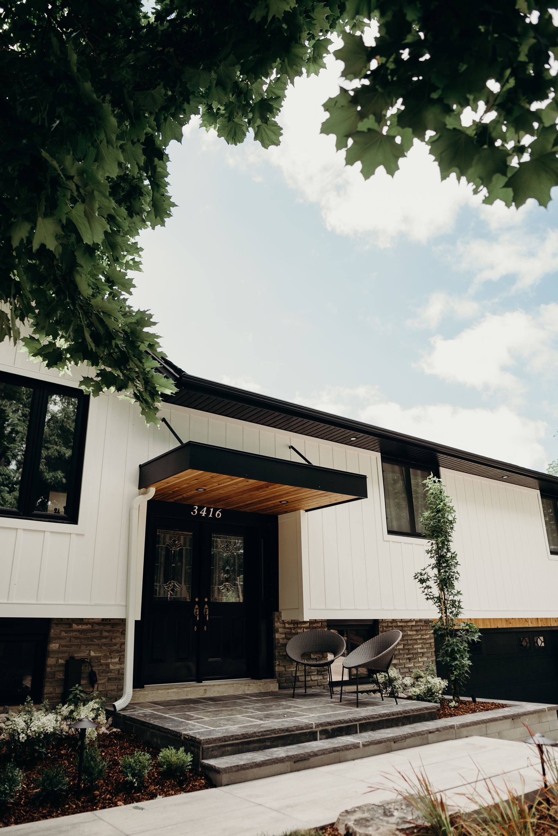A white house with a black door and a porch with chairs and a table.