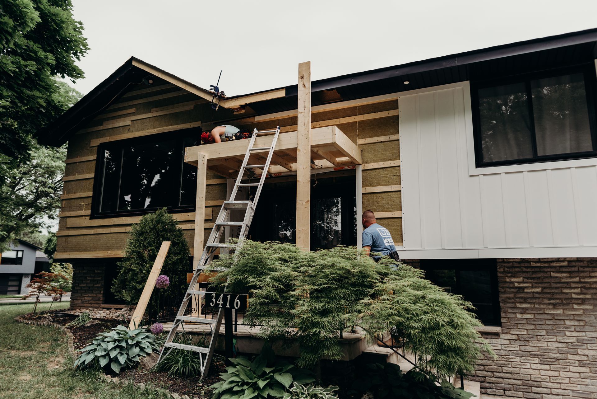 A man is standing on a ladder in front of a house.