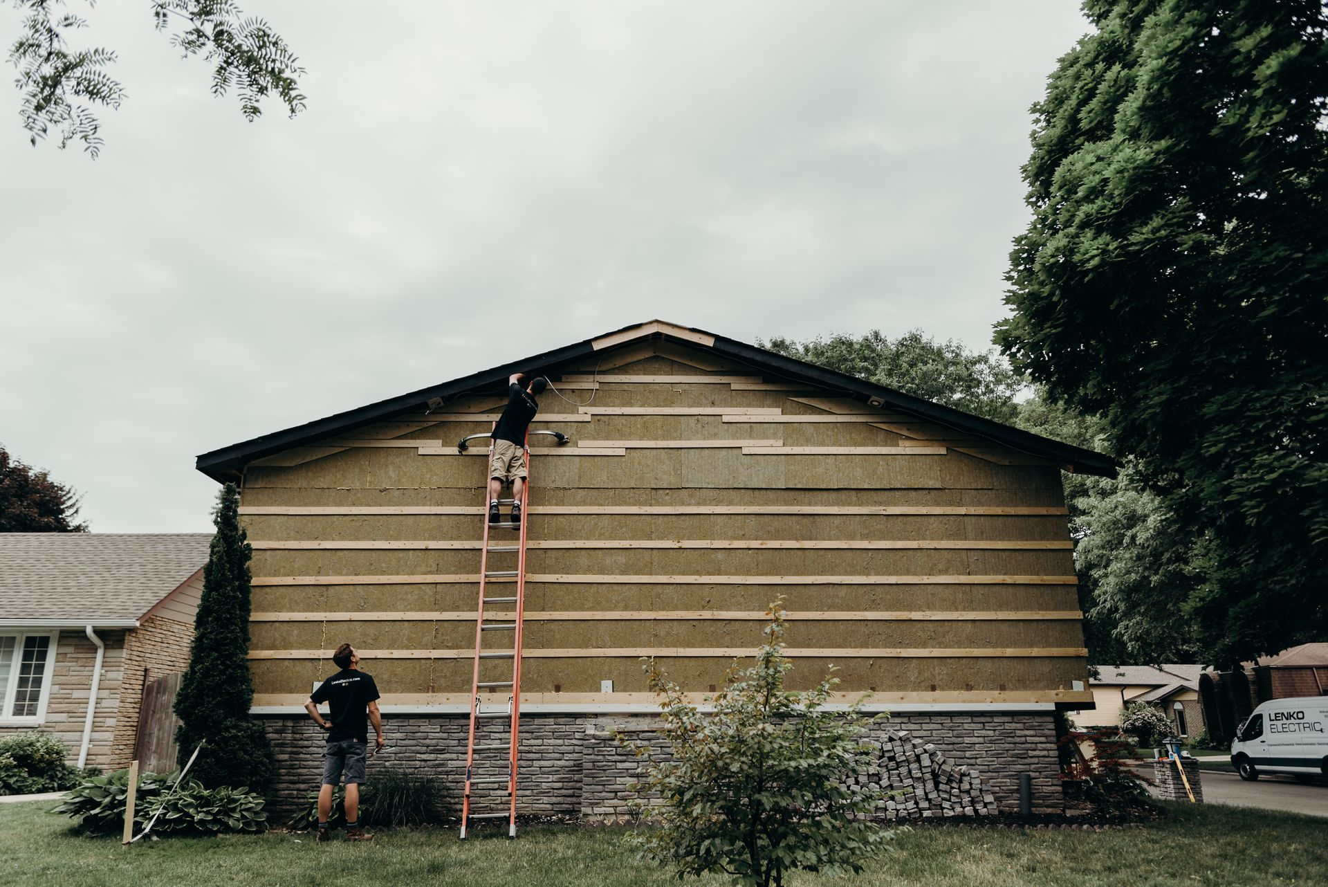 A man on a ladder is working on the side of a house.