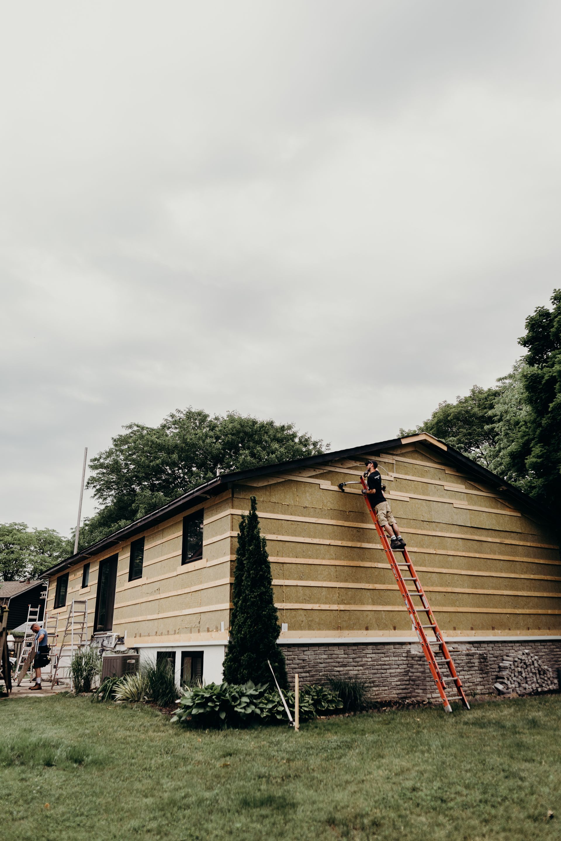 A man is standing on a ladder on the side of a house.