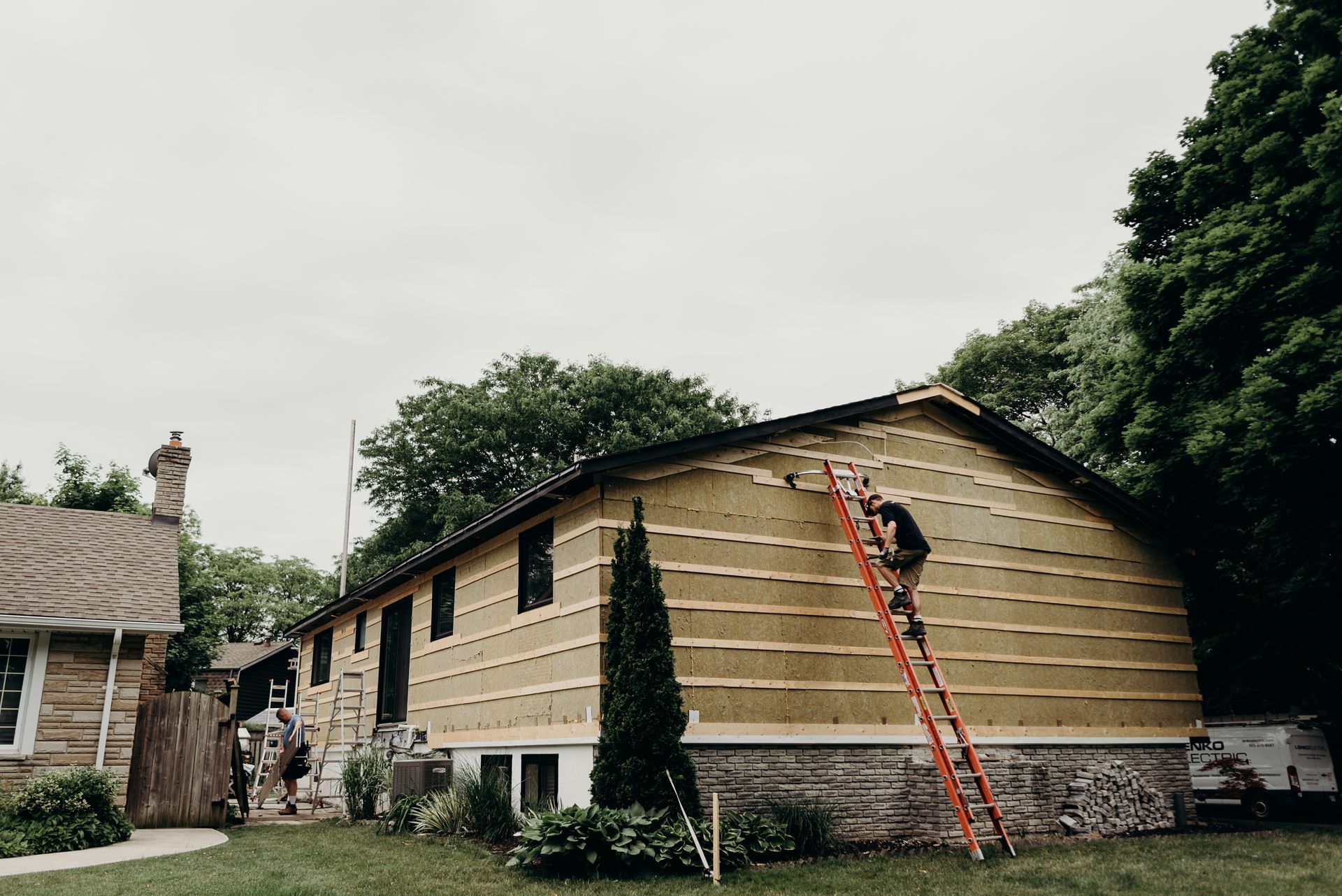 A man is standing on a ladder on the side of a house.