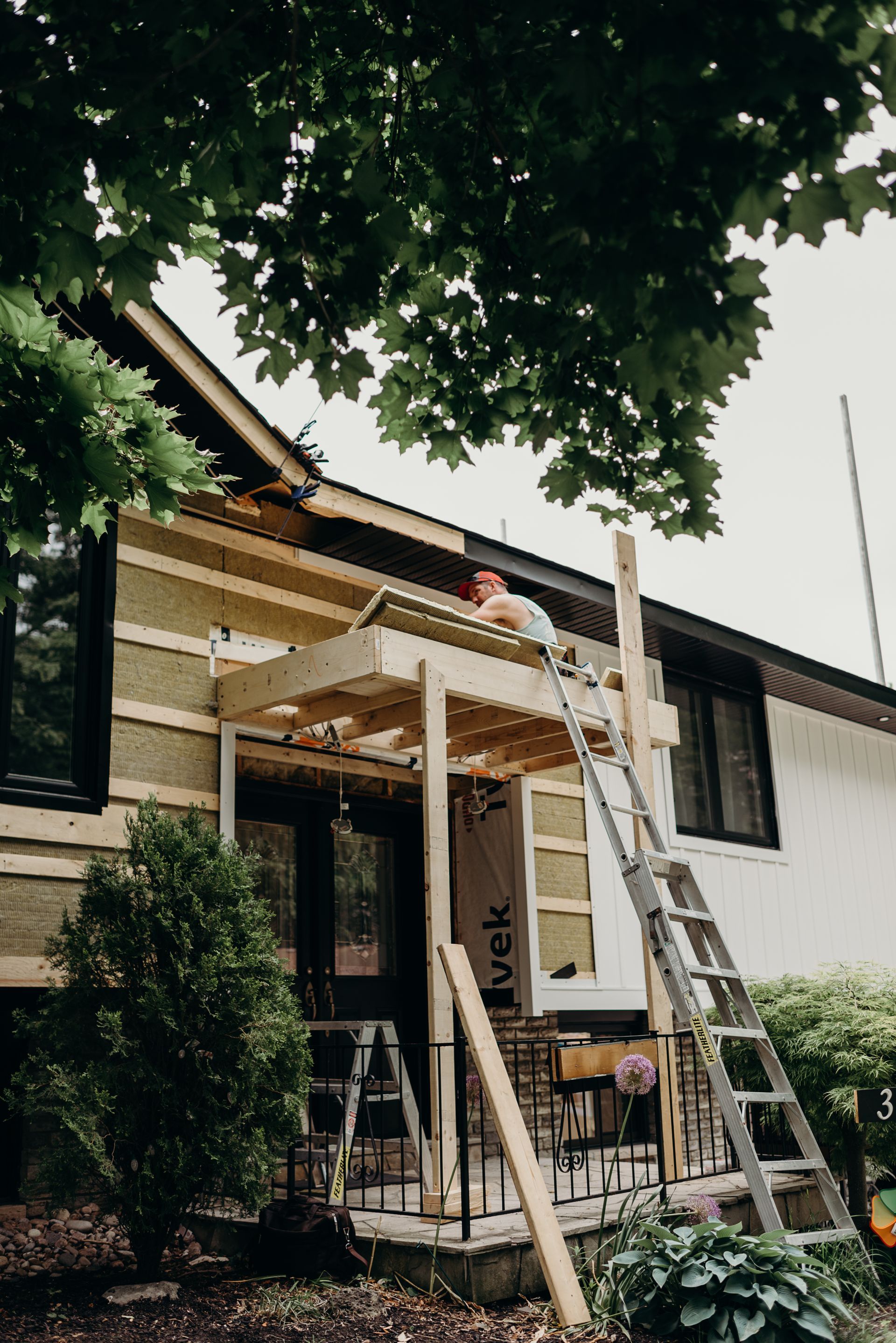 A man on a ladder is working on the roof of a house.