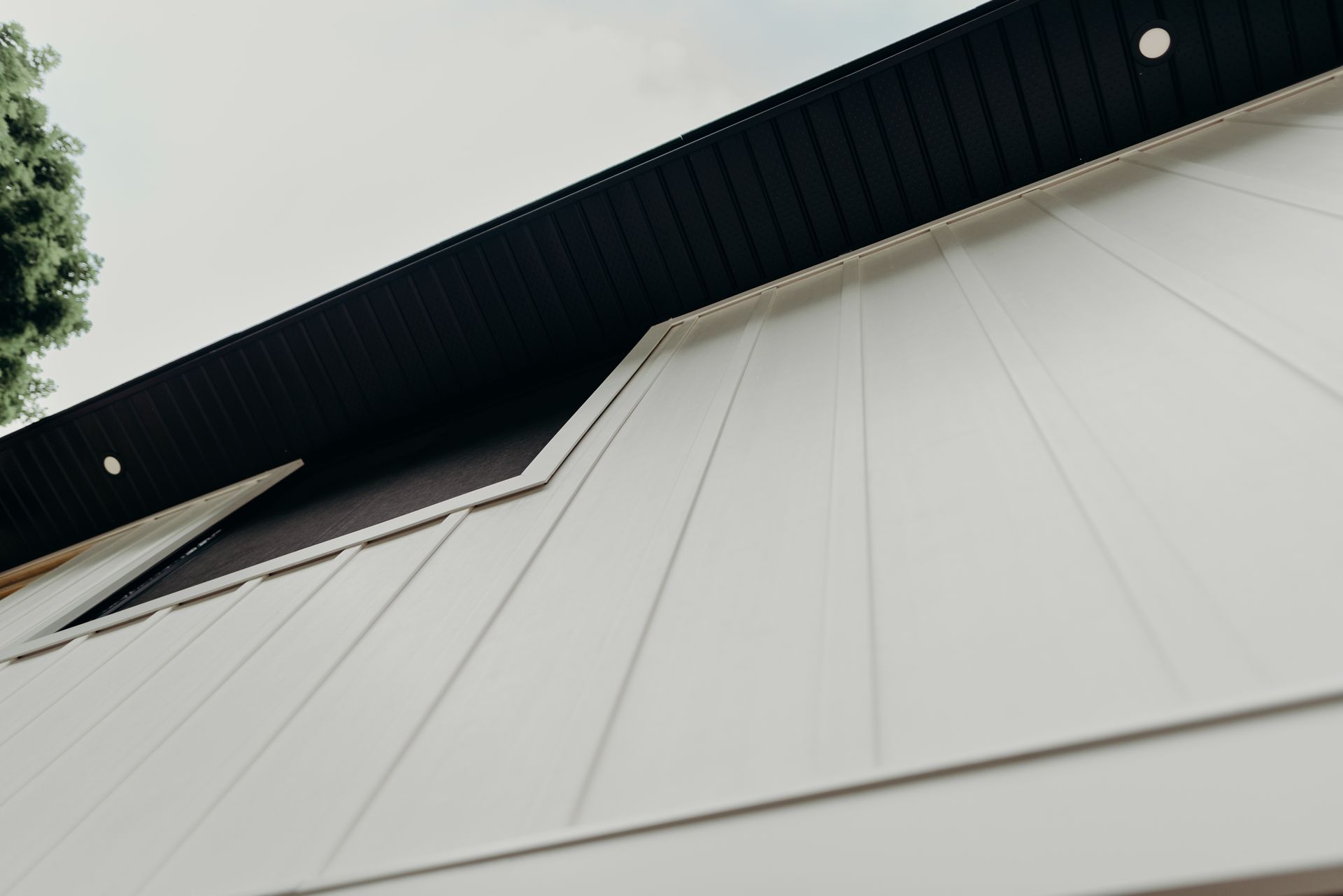 A white building with a black roof and a tree in the background.