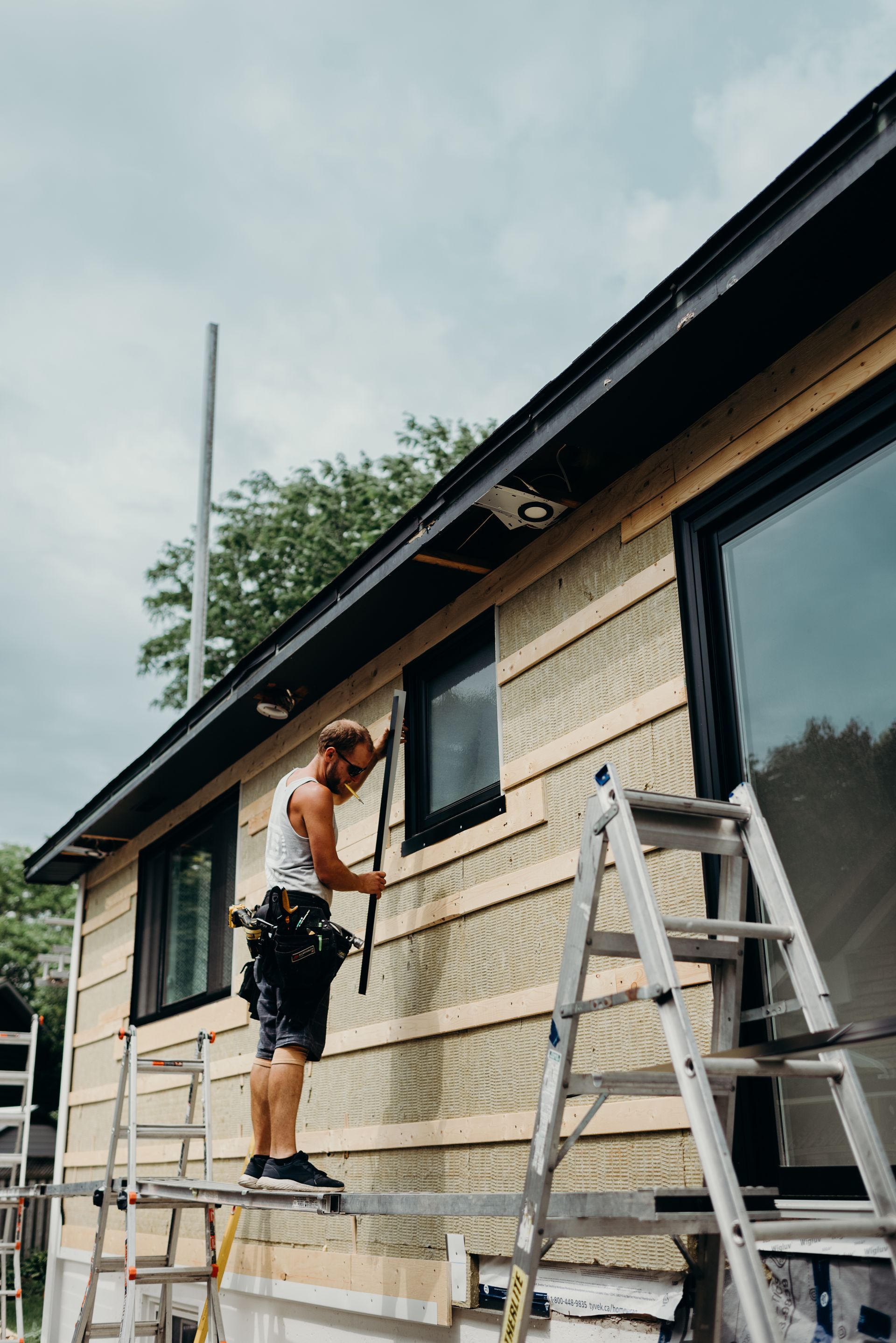 A man is standing on a ladder working on the side of a house.