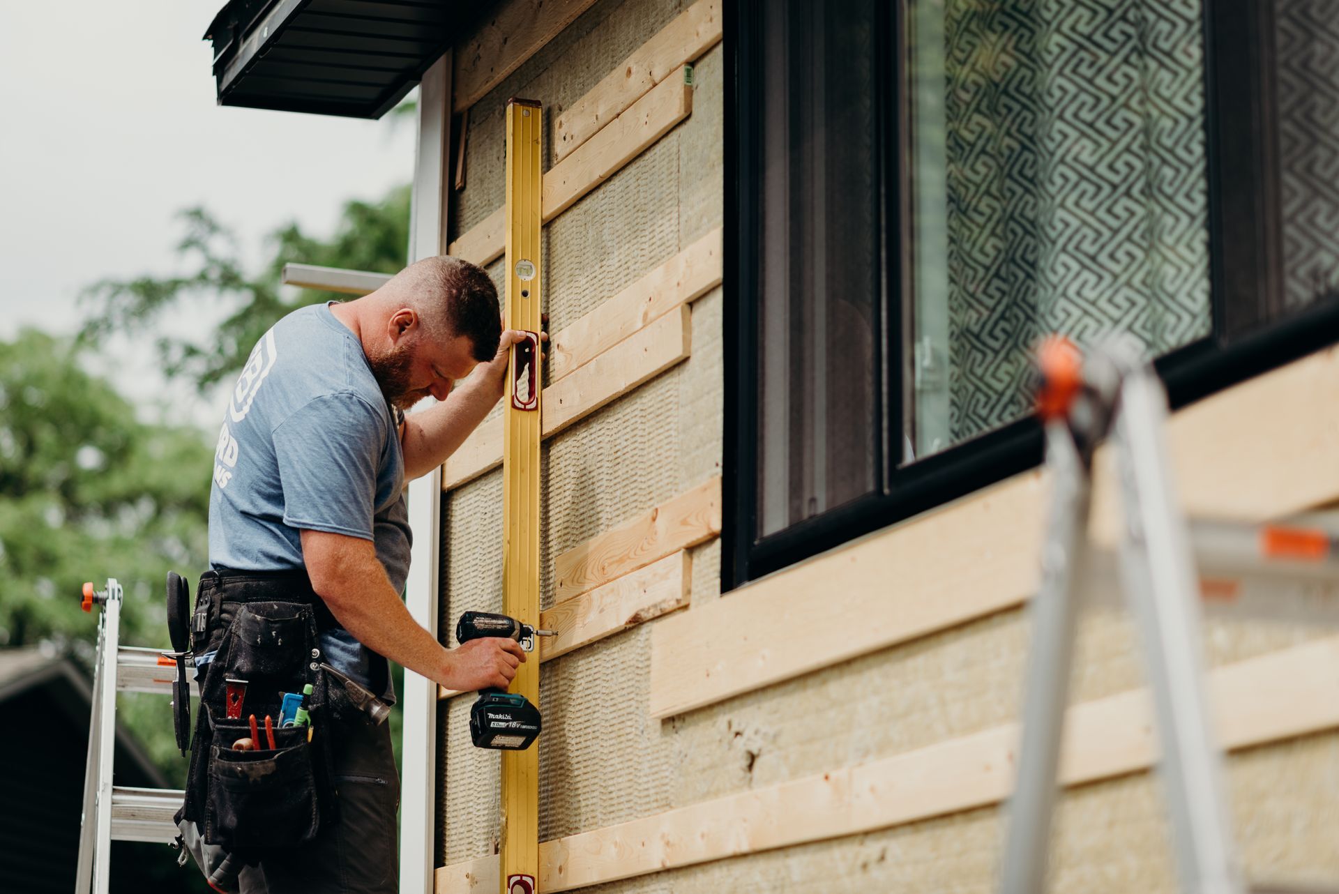 A man is standing on a ladder measuring a wall with a level.