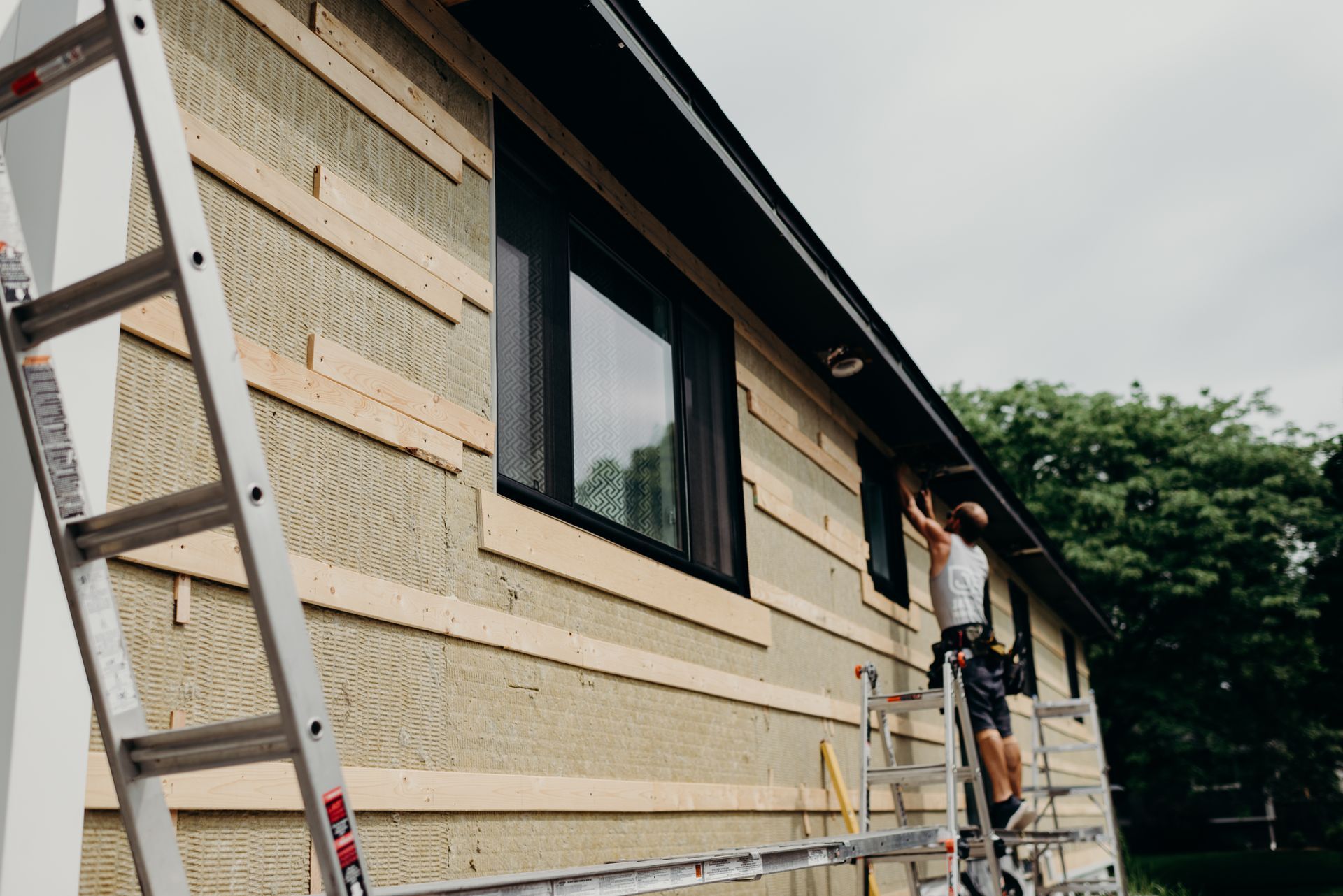 A man is standing on a ladder on the side of a house.