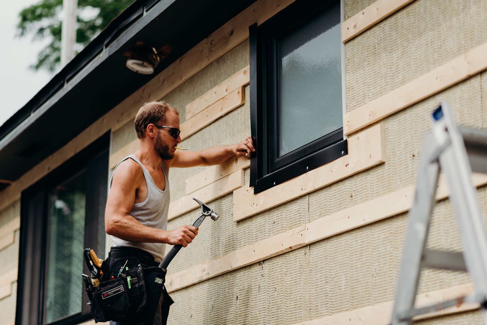 A man is standing on a ladder fixing a window on a house.