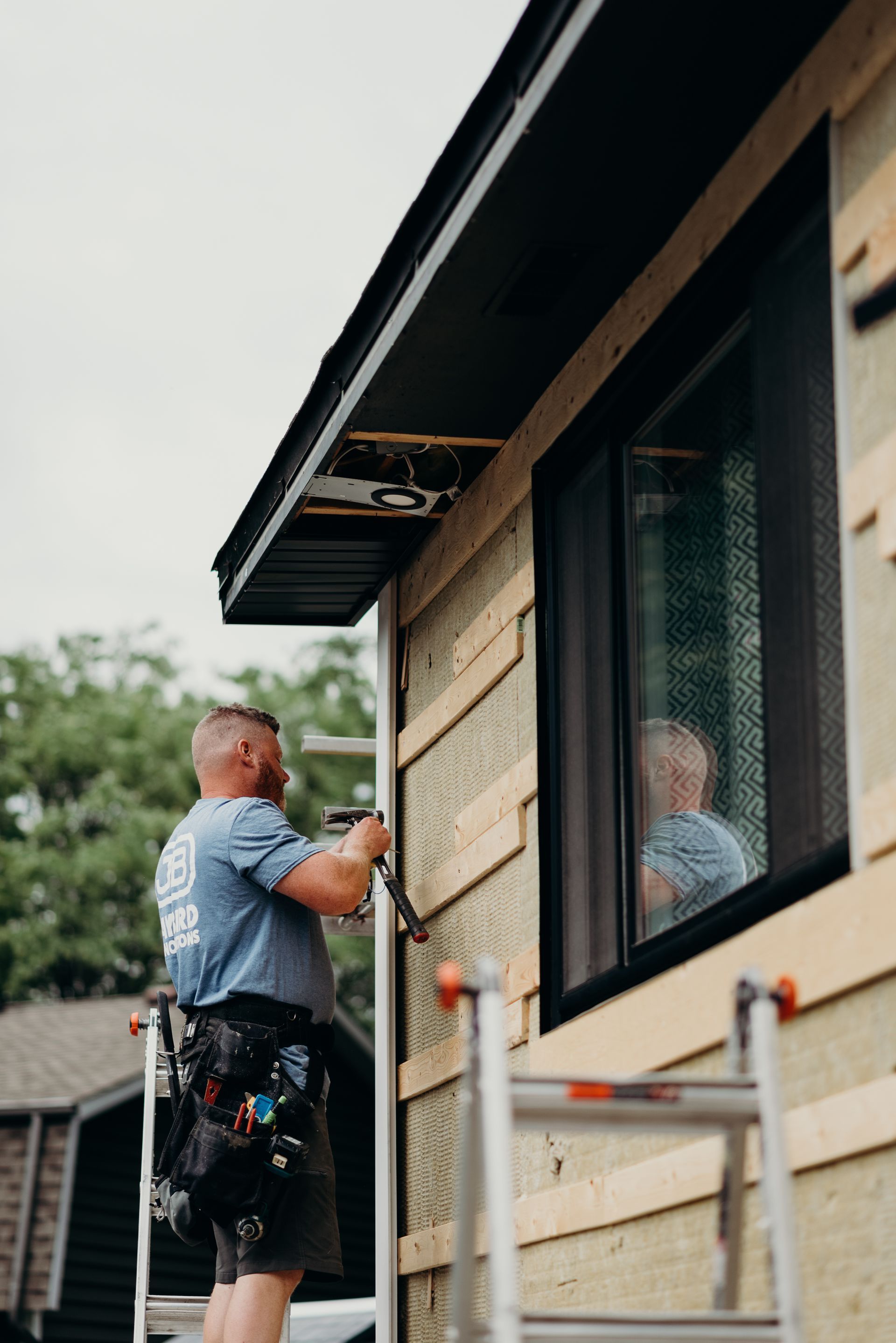 A man is standing on a ladder fixing a window on a house.