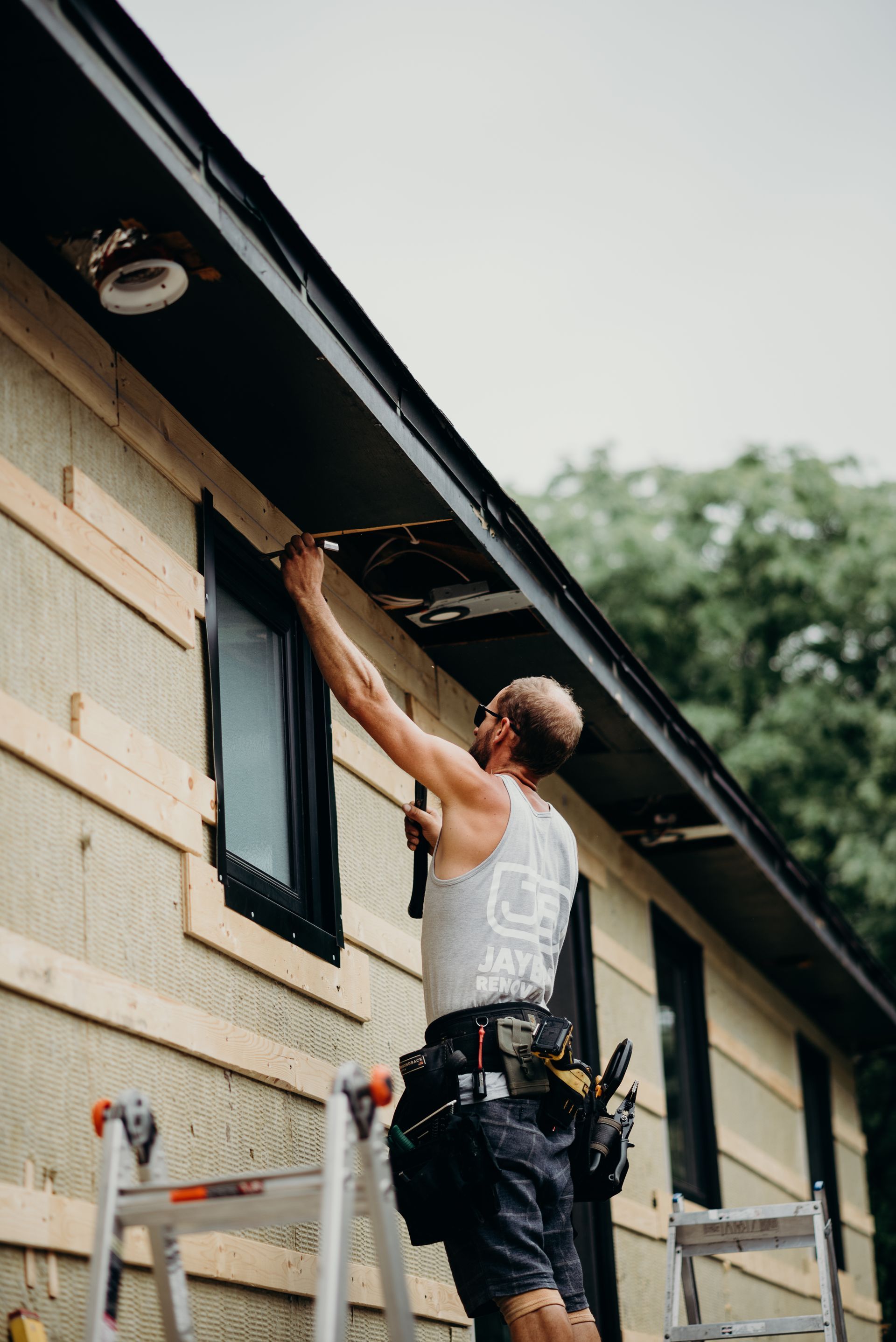 A man is standing on a ladder fixing a window on a house.