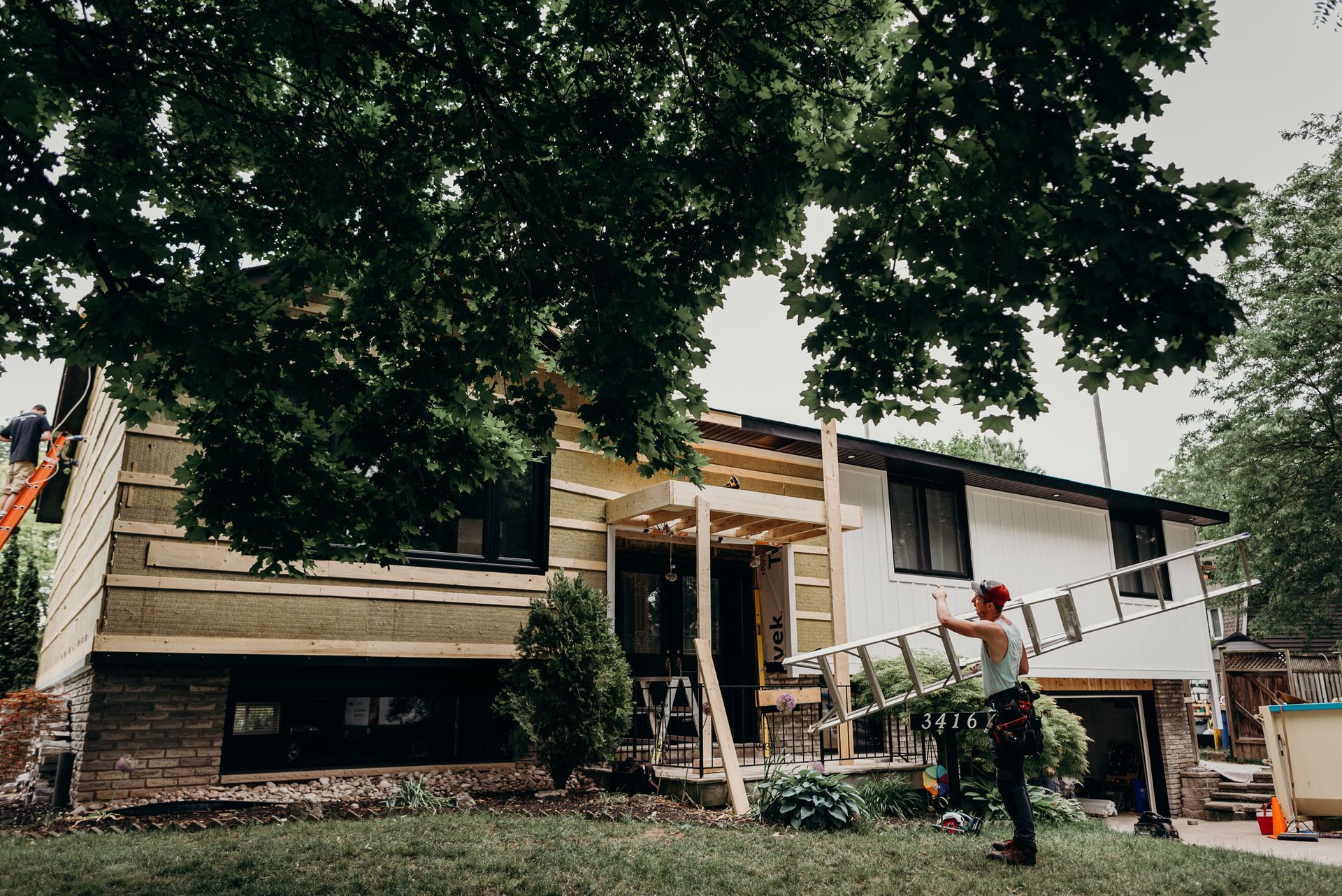 A man is standing in front of a house holding a ladder.