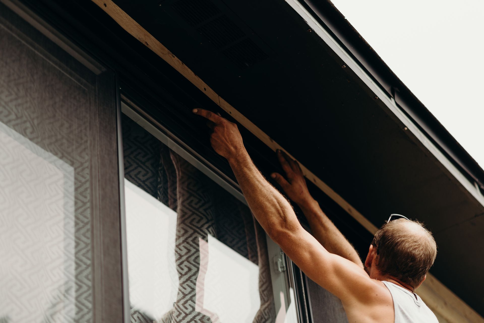 A man without a shirt is working on a window