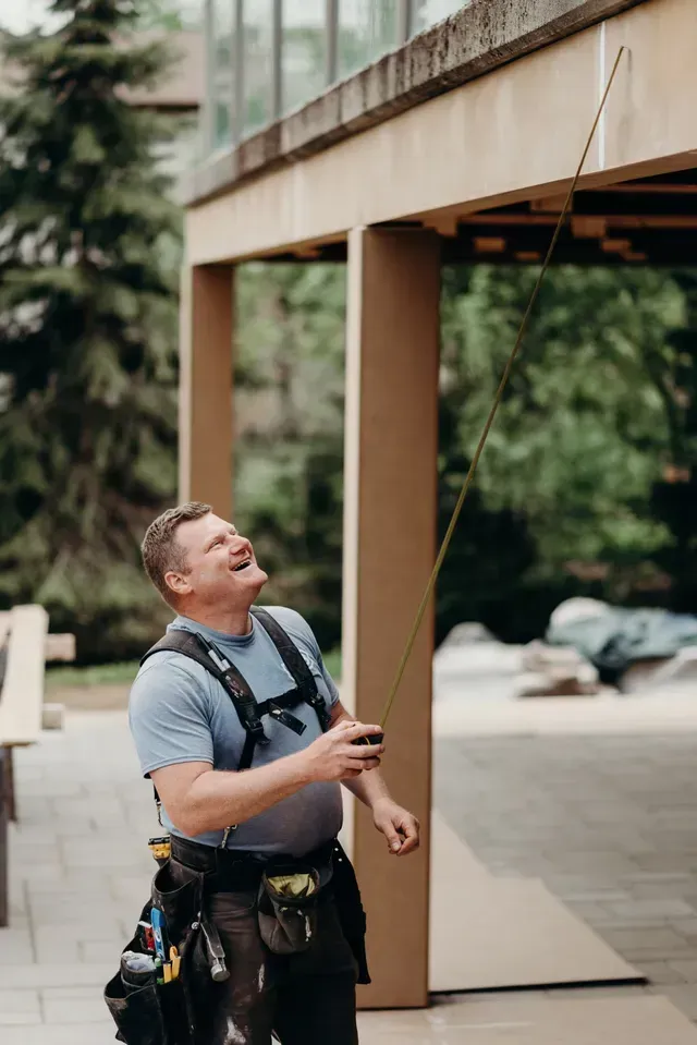 Man on a patio using a long tool to inspect the underside of a roof overhang.