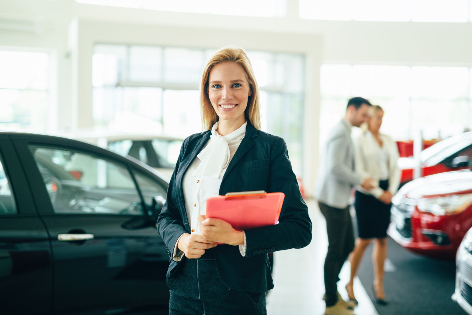 A woman is holding a clipboard in a car showroom.