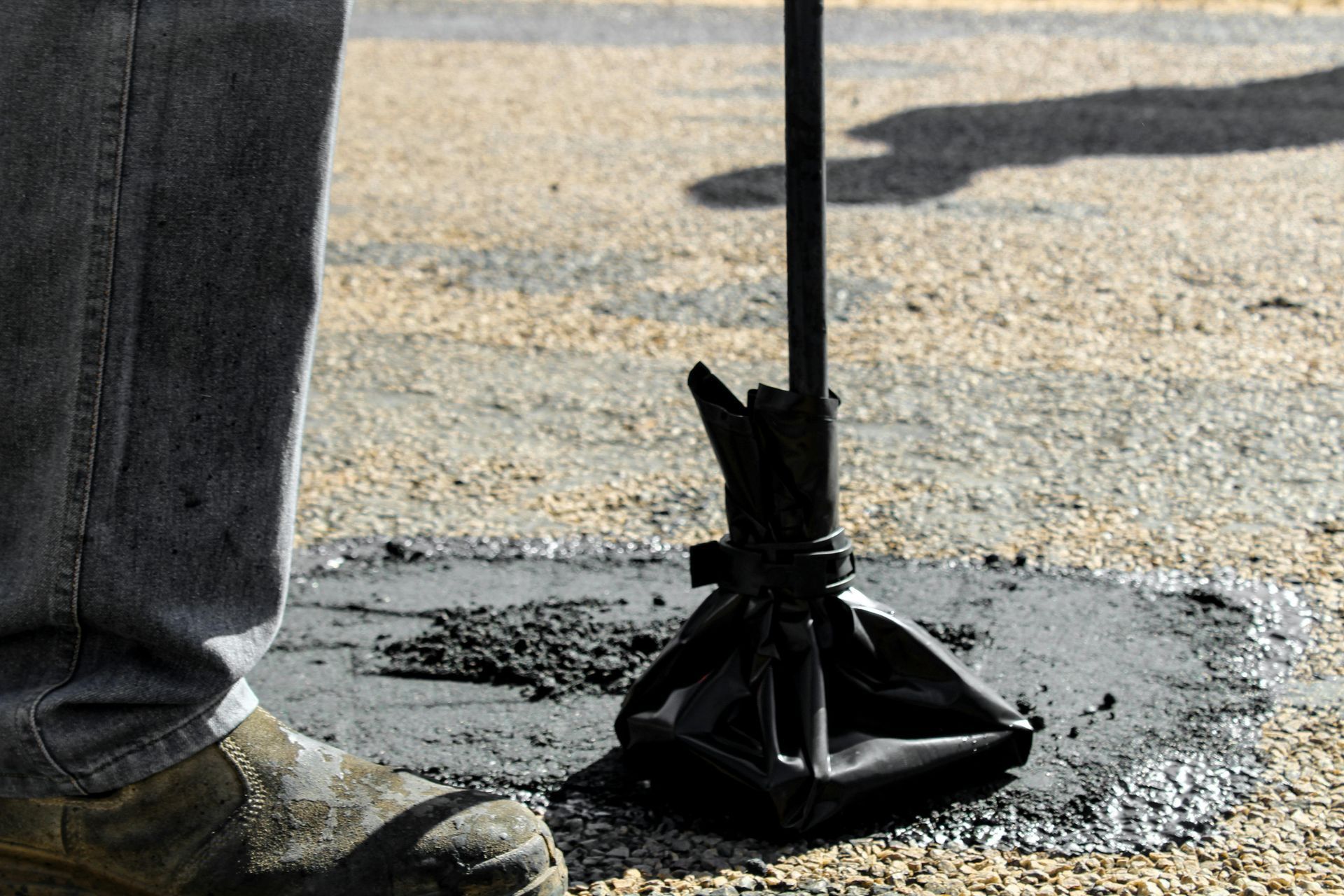 Person using a jackhammer on asphalt, with boots and a black drill bit visible.