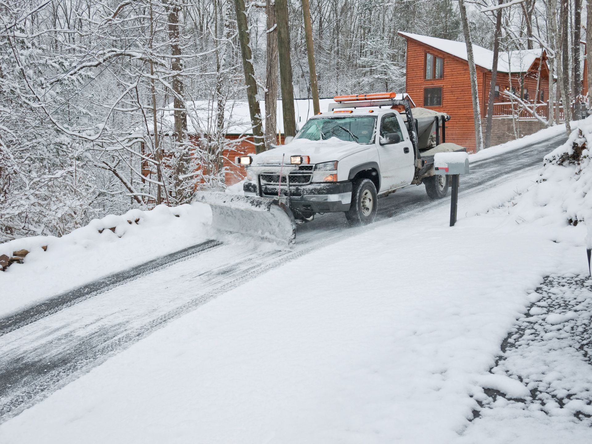 A snow plow is driving down a snow covered road.