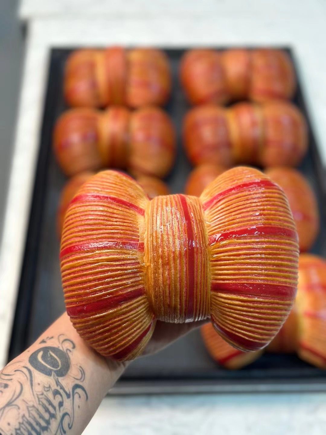 Une personne tient un pain en forme de nœud papillon devant un plateau de pain.